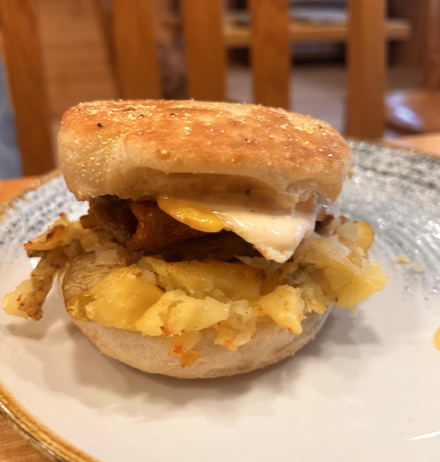 Close-up of  Bacon, egg and cheese breakfast sandwich with fried egg, bacon, and cheese on a toasted English muffin, served on a ceramic plate.