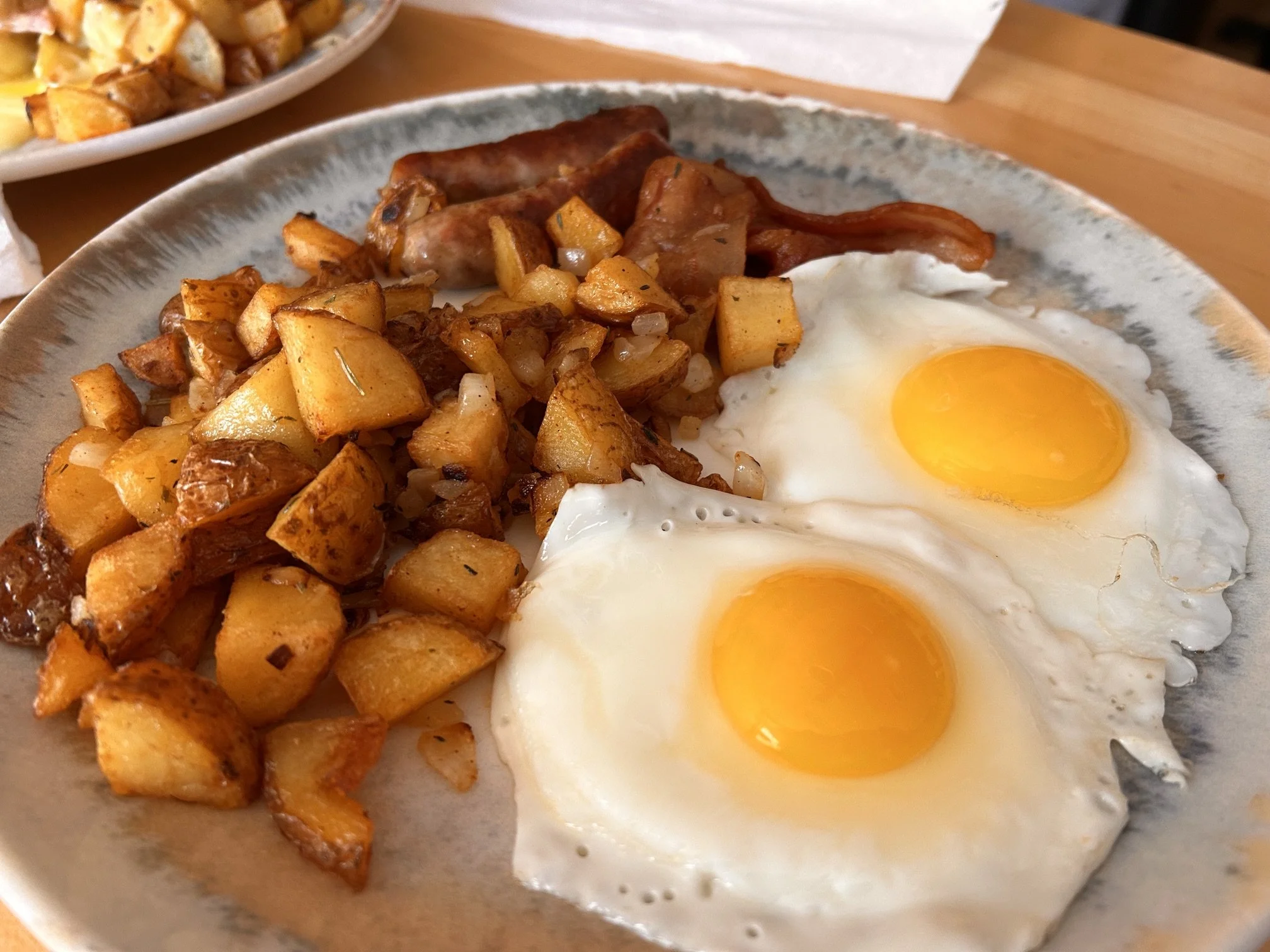 Fried eggs with runny yolks, roasted breakfast potatoes, and crispy bacon on a ceramic plate.