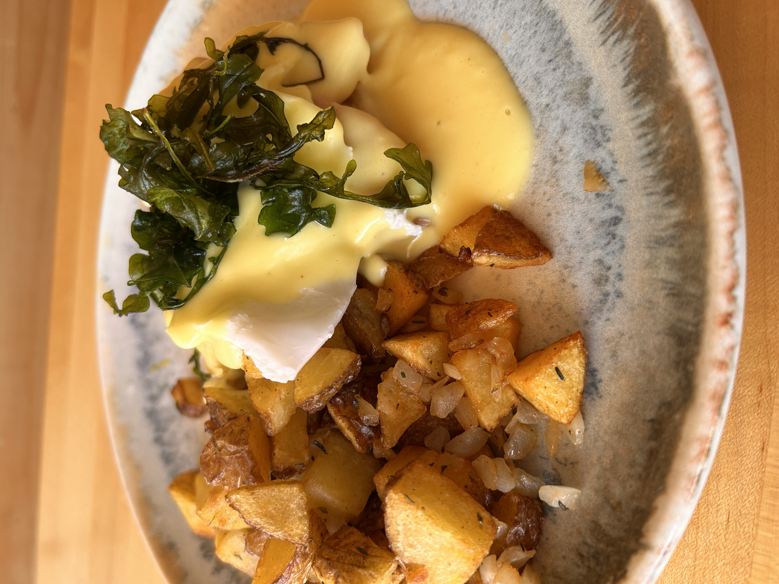A breakfast plate with eggs Benedict, crispy potatoes, greens, and homemade ham