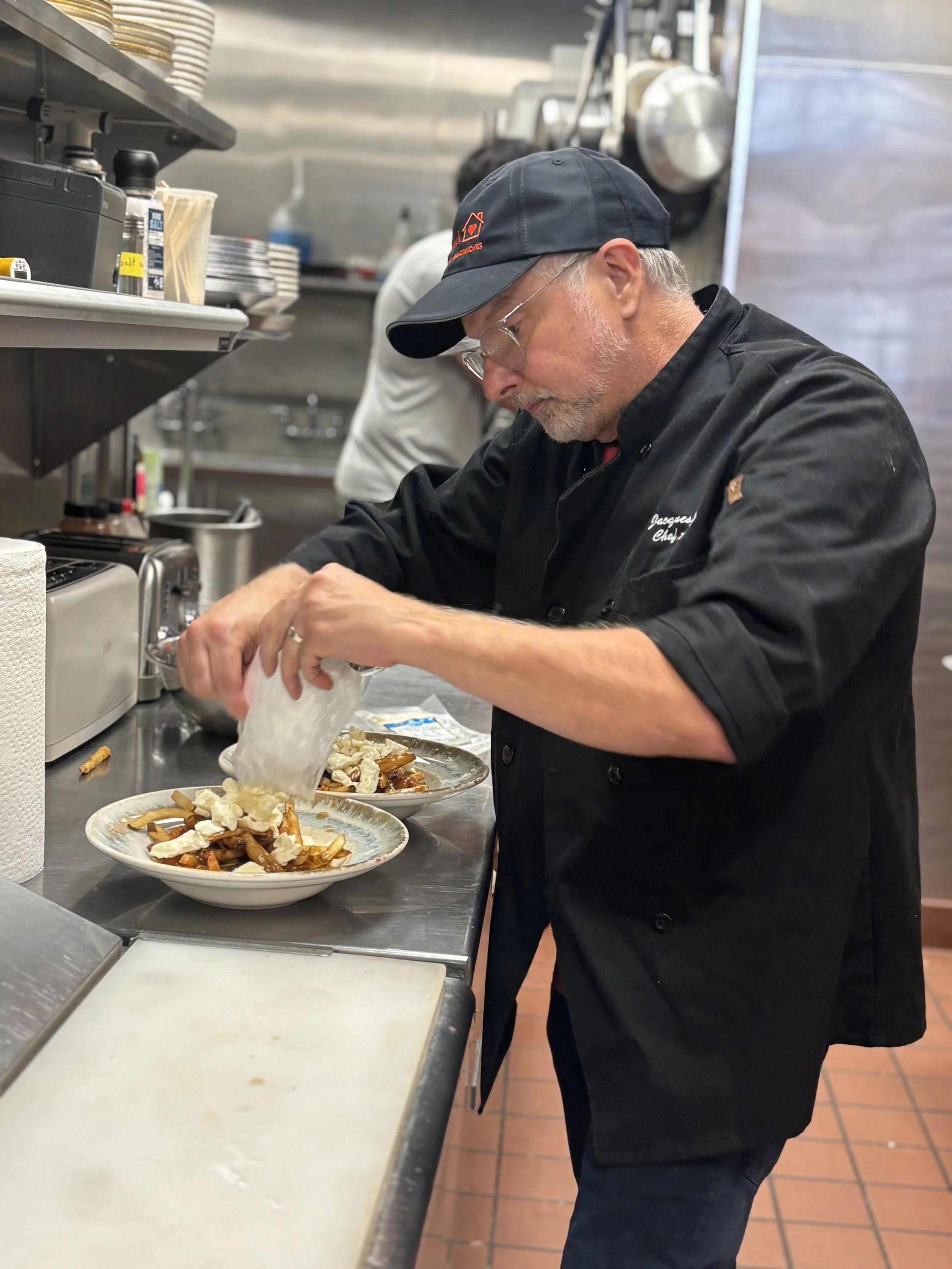 Jack, the chef,  preparing a lunch dish in a commercial kitchen, adding ingredients to a bowl on a stainless steel counter.