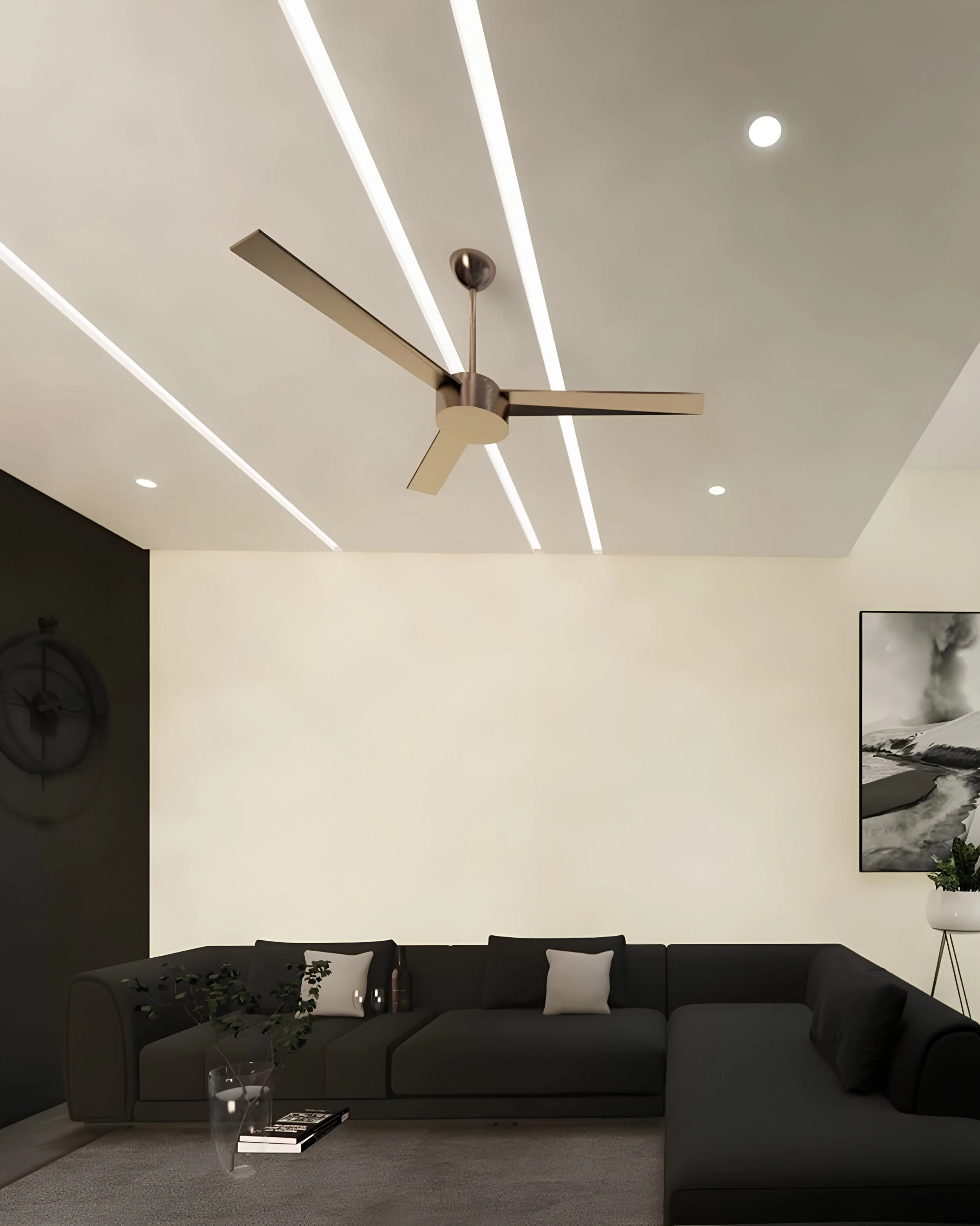 Modern living room with a large gray sectional sofa, black throw pillow, glass side table holding a glass of water and magazines, a dark wall clock, and minimalist decor. A large framed black and white photograph of mountains hangs to the right. The 