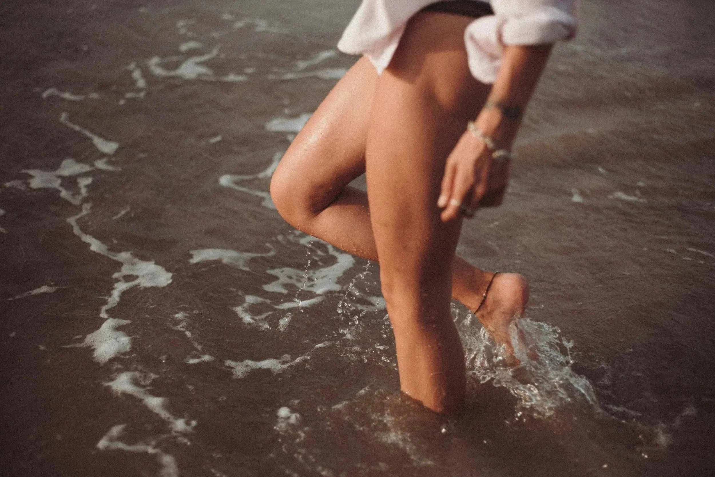 Person walking through shallow ocean water with warm sunset lighting.