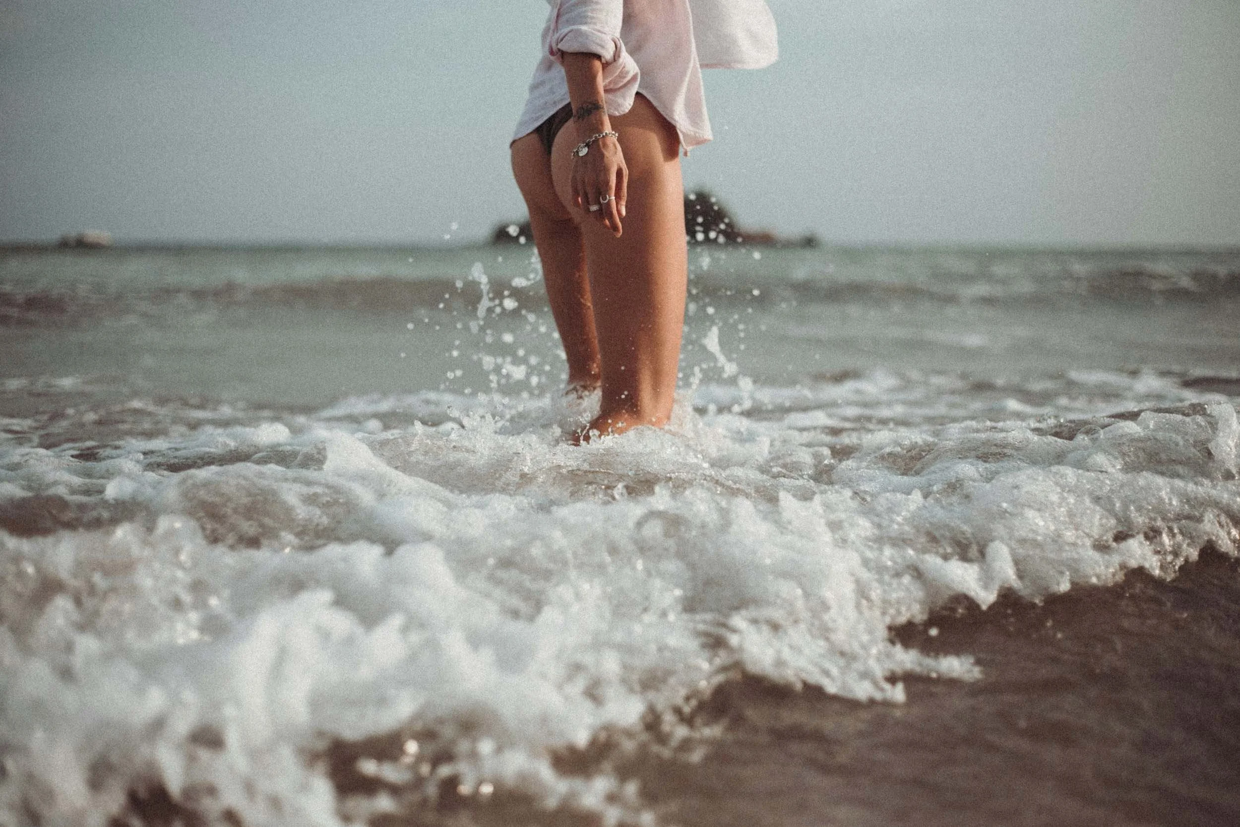 Person walking through shallow ocean water with warm sunset lighting.