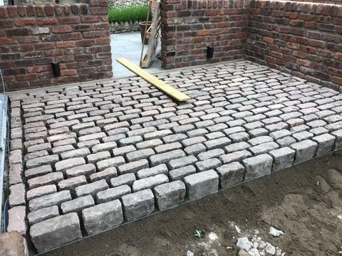 New cobblestone paving in progress on a brick patio with a wooden level tool placed on the stones.