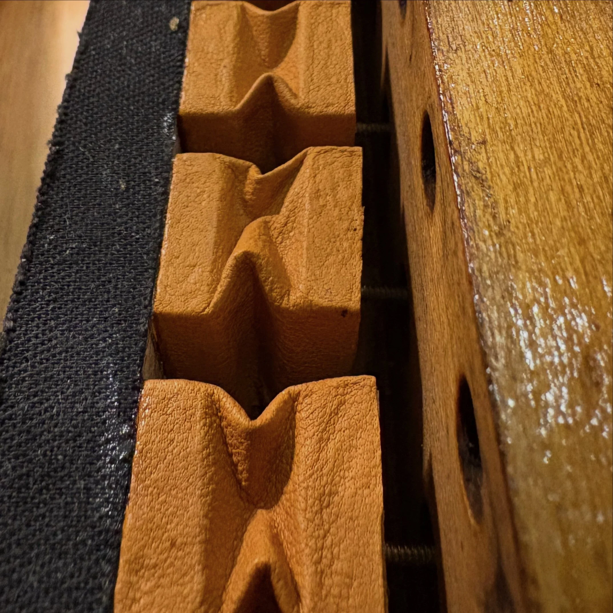 Close-up view of several square leather-covered pneumatics attached to a wooden surface, with black rubber cloth on the left side.