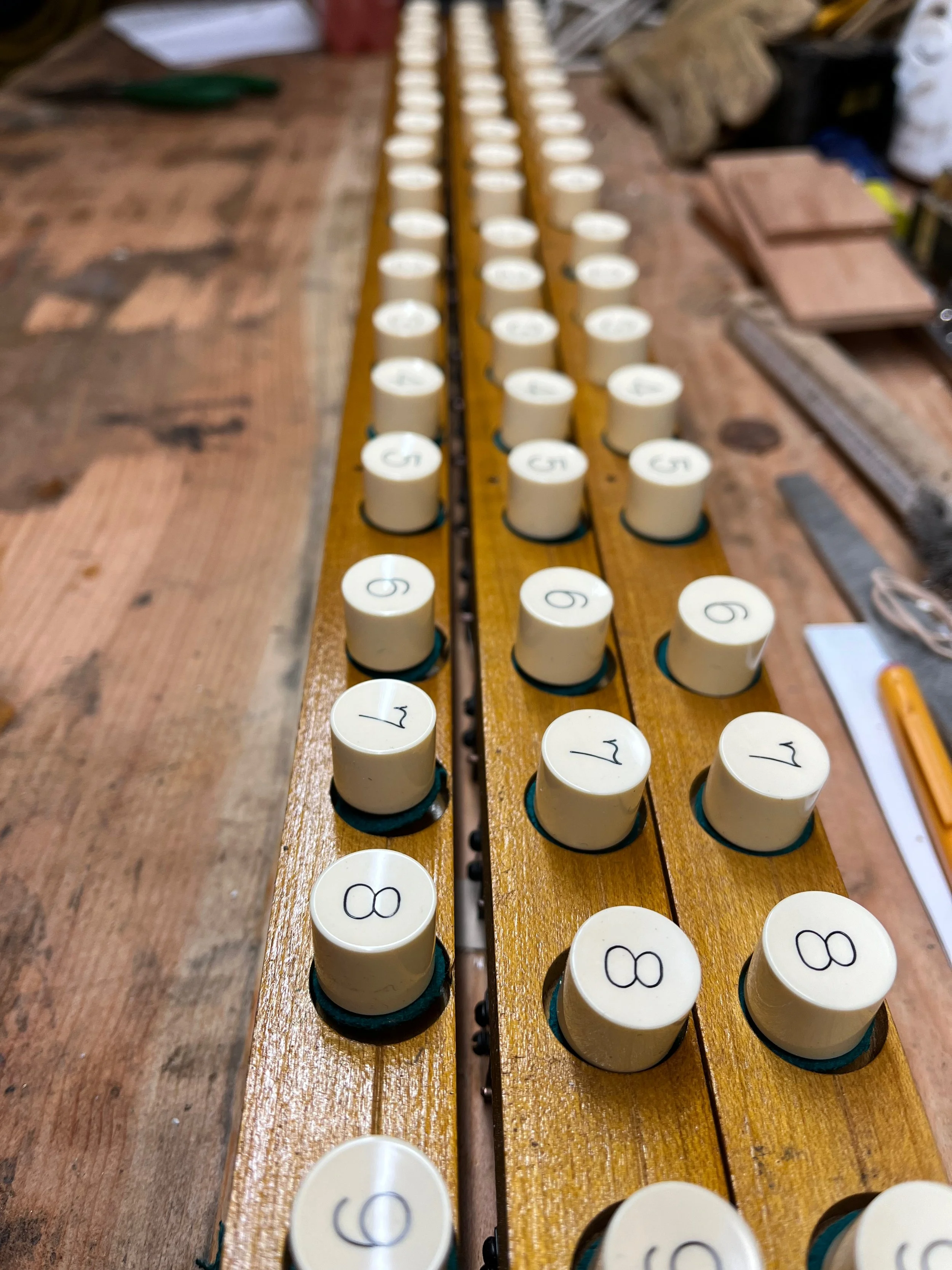Close-up of replica organ piston rails with beige numbered knobs in a workshop setting.