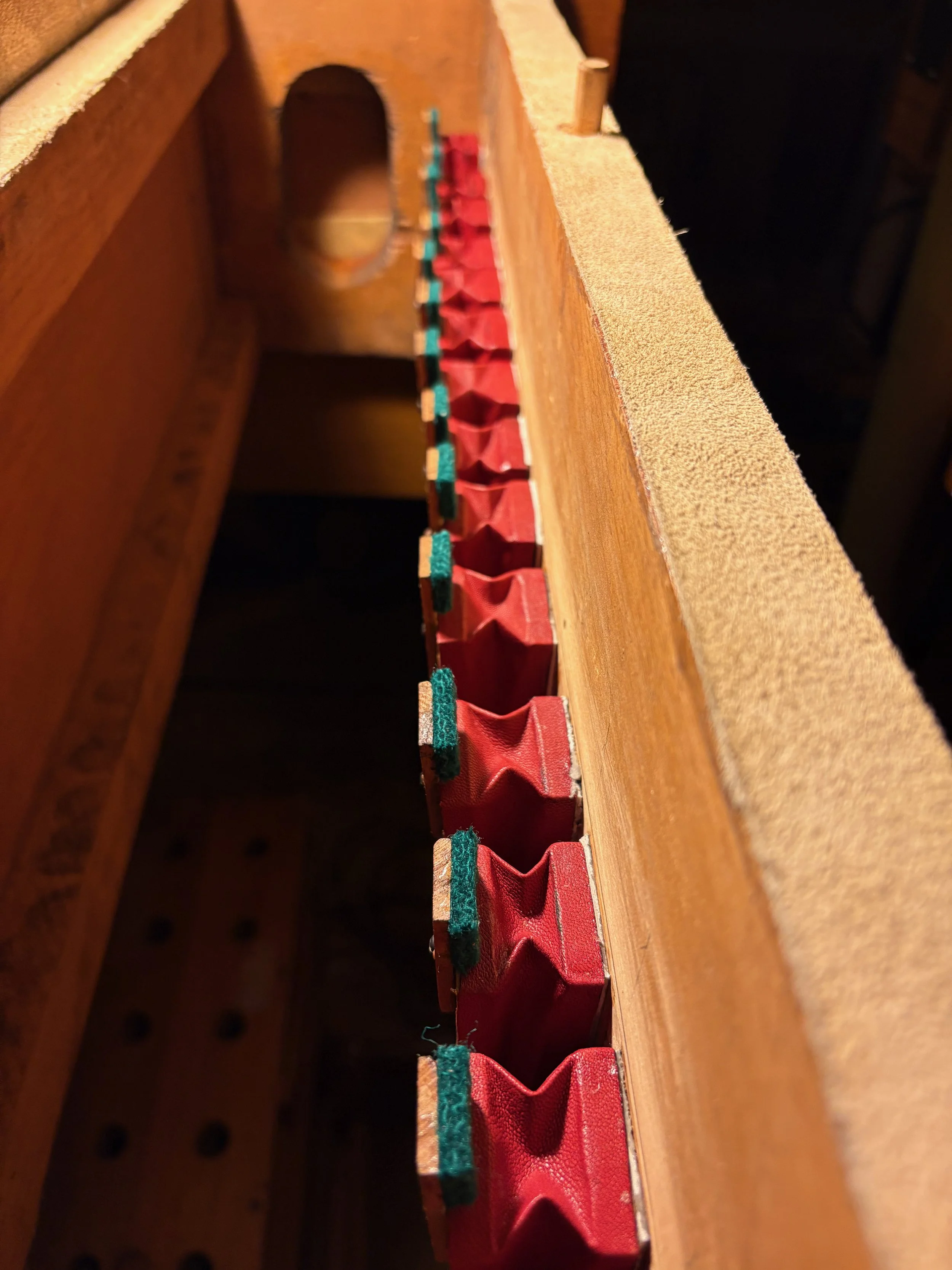 Close-up of a vintage wooden organ pipe chest with red leather pneumatics and green felt bumpers.