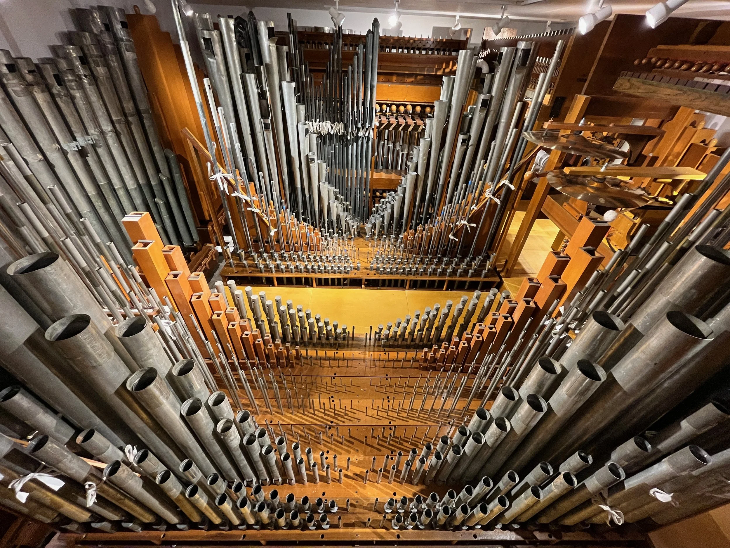 The image shows an intricate organ pipe structure from a top angle, revealing many metal and wood pipes of varying lengths and diameters. The pipes are arranged in an orderly manner within a wooden frame, part of a pipe organ.