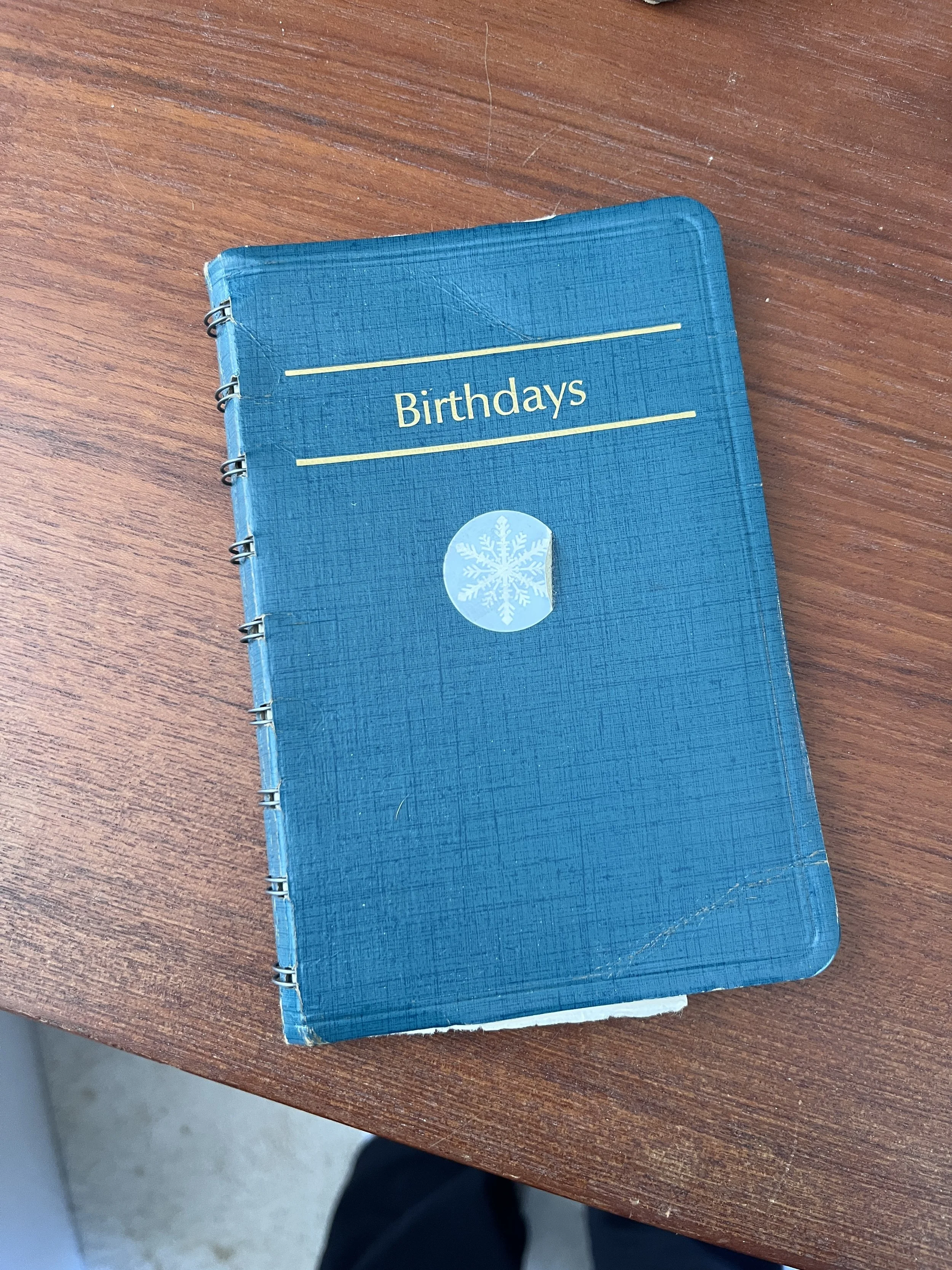 A small green notebook titled 'Birthdays' with a snowflake sticker on the cover, placed on a wooden surface.