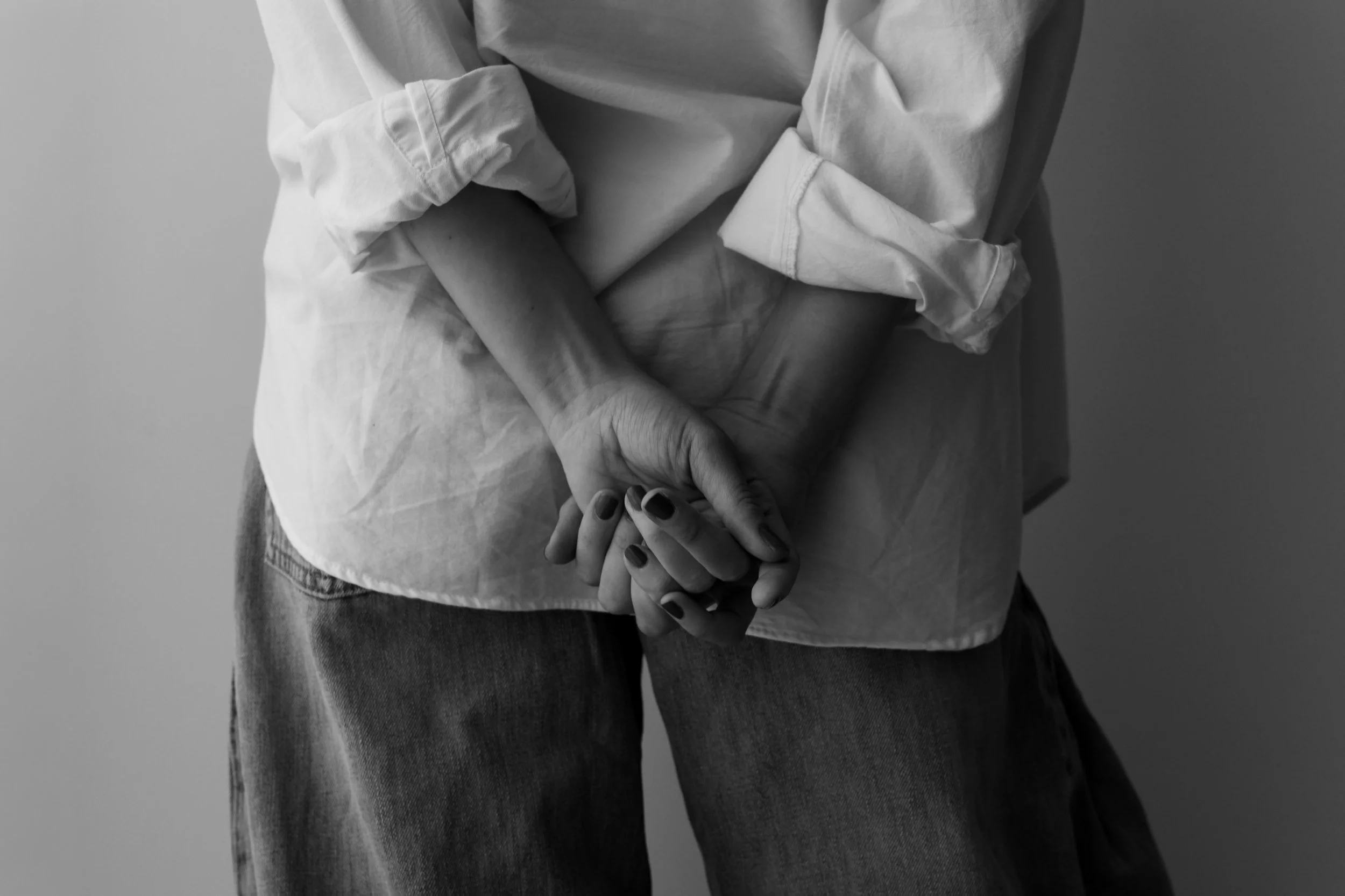 A person wearing a light-colored long-sleeve shirt with rolled-up sleeves, holding hands with another person. The image is in black and white, focusing on their hands and part of their torsos.