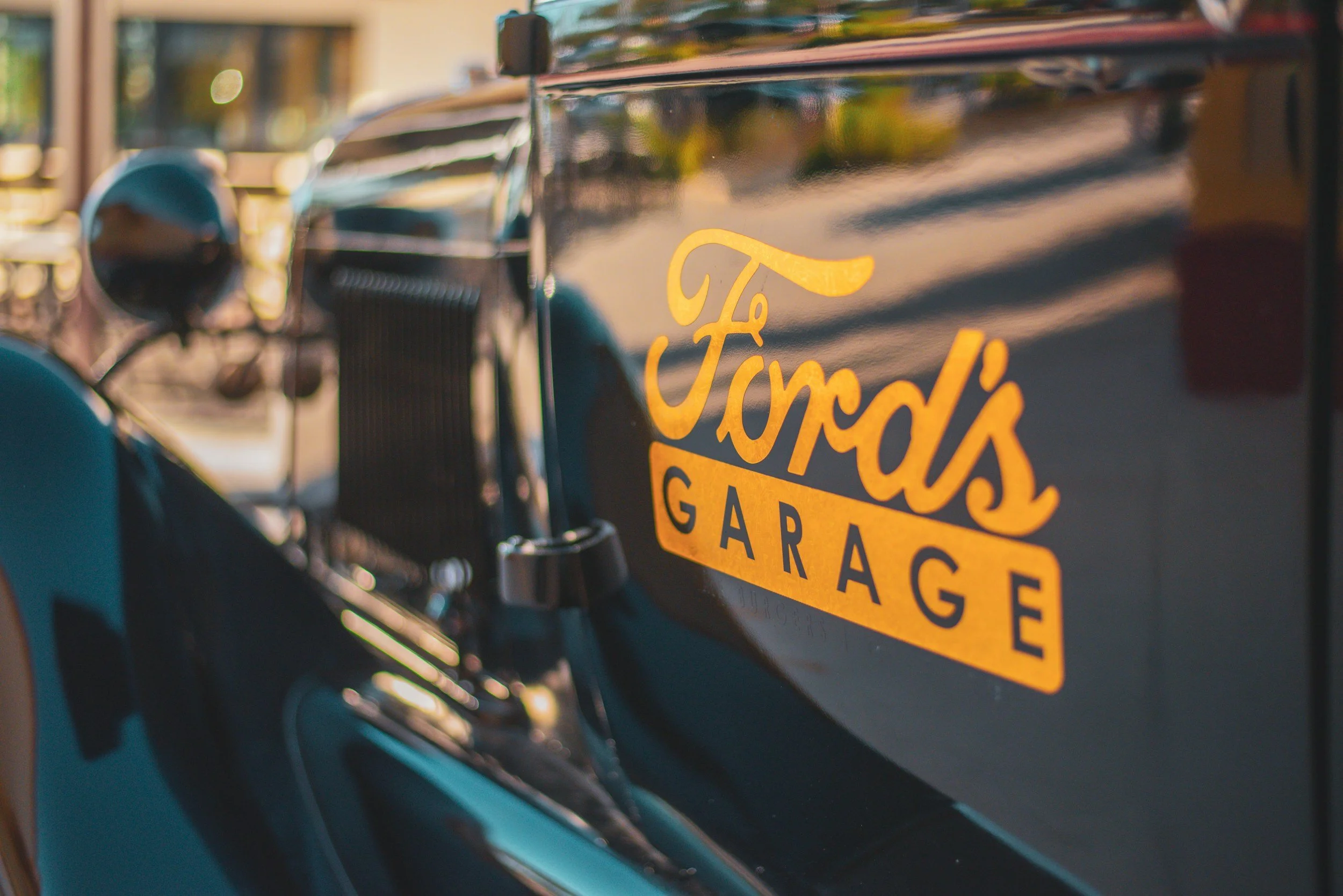 Close-up of a vintage black car with yellow lettering that says 'Fords Garage' on the side.