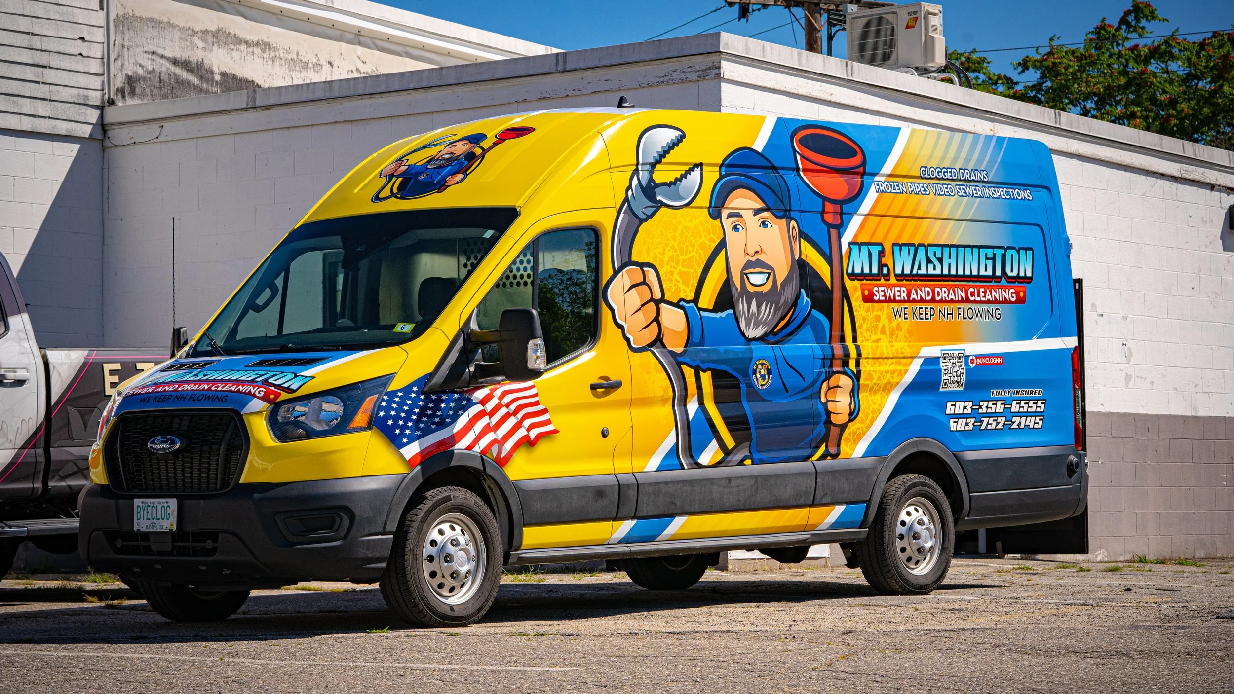A colorful service van for sewer and drain cleaning with cartoon graphics of a worker holding a wrench and an illustration of a man in a uniform holding a plunger. The van features an American flag, contact information, and a QR code, parked next to a white wall and a tree with blue sky above.