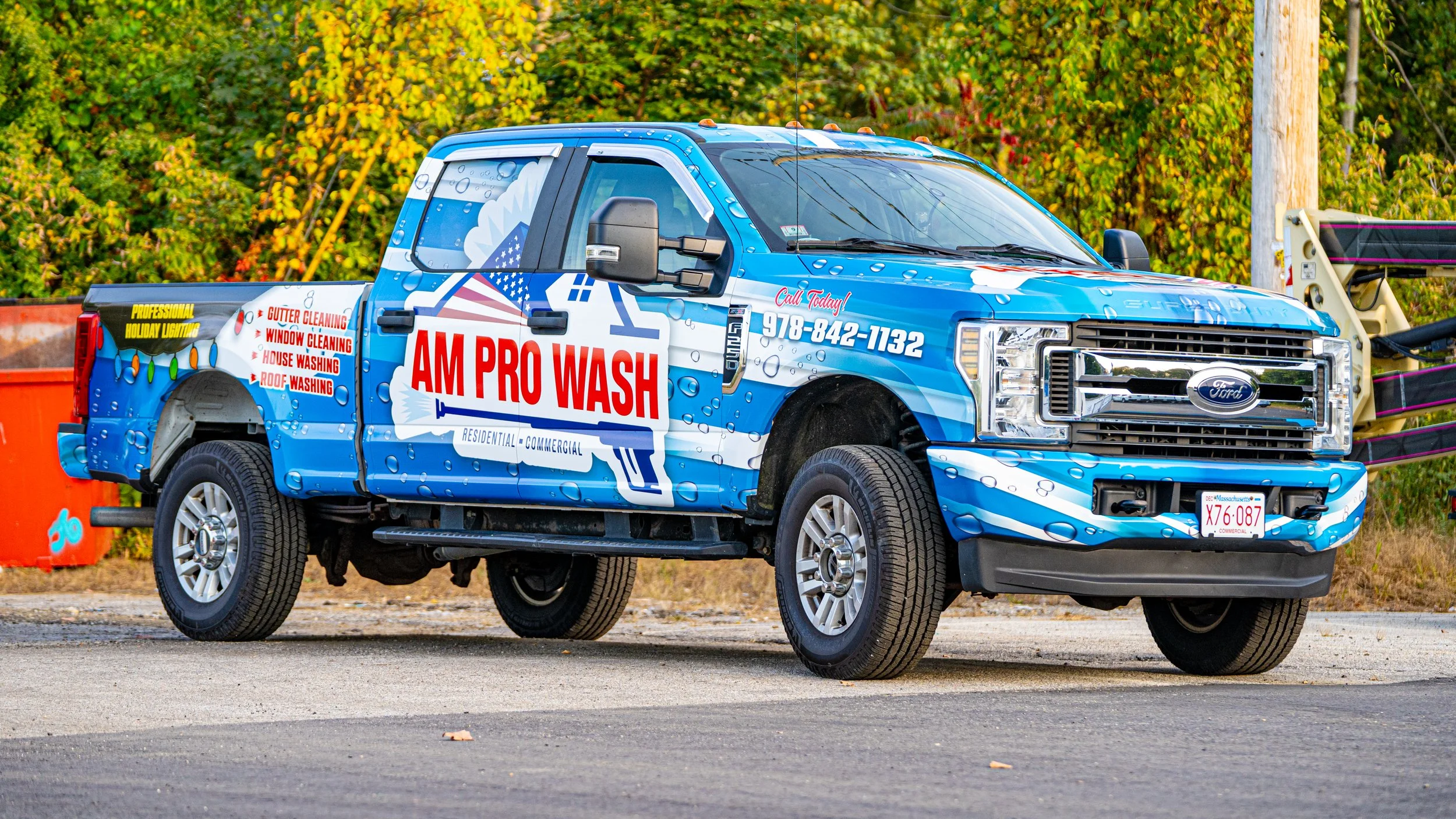 Blue pickup truck with Am Pro Wash advertising, parked on roadside with fall foliage in background.