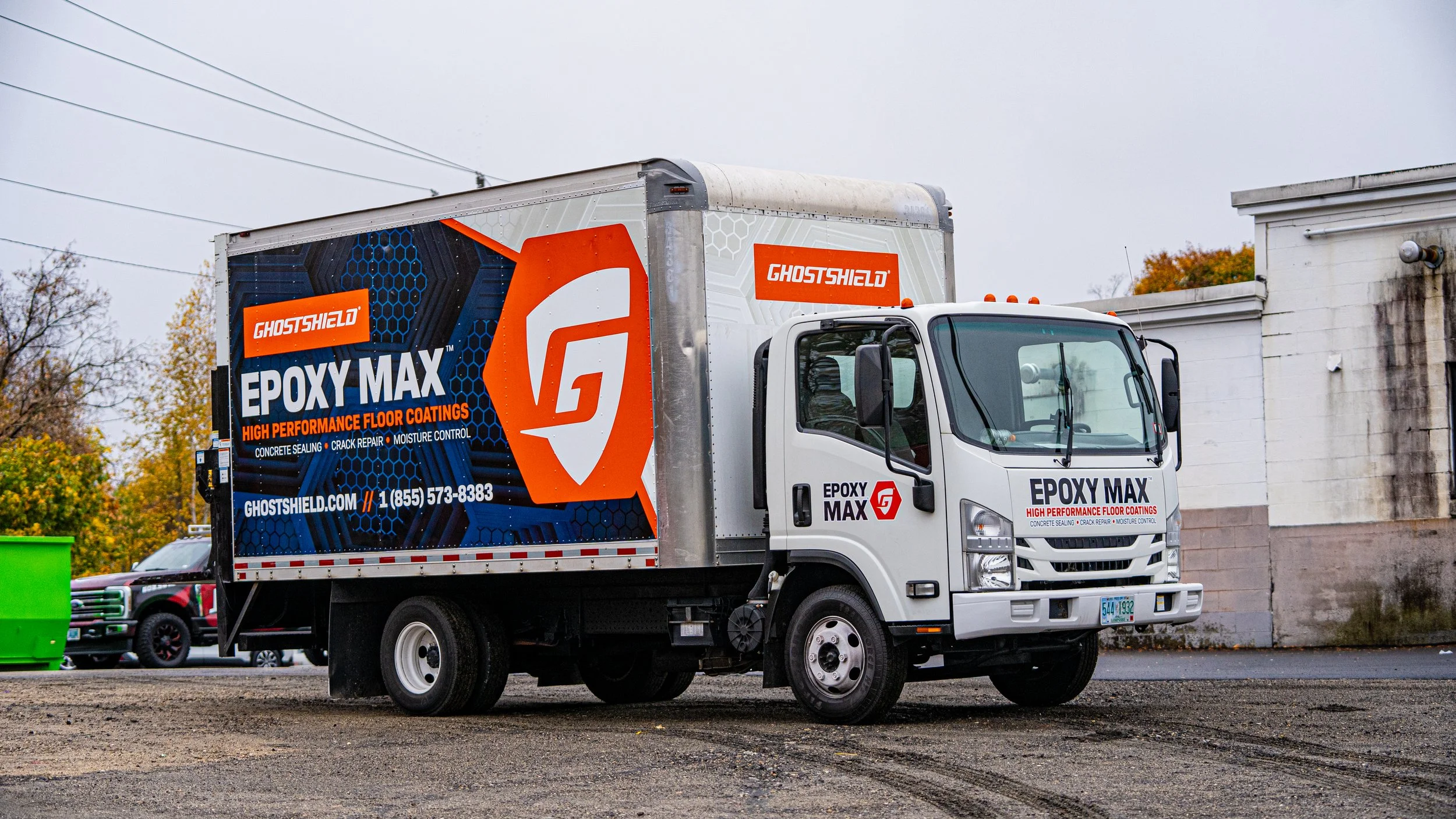 A delivery truck promoting GhostShield Epoxy Max high-performance floor coatings parked in an urban area with autumn trees in the background.