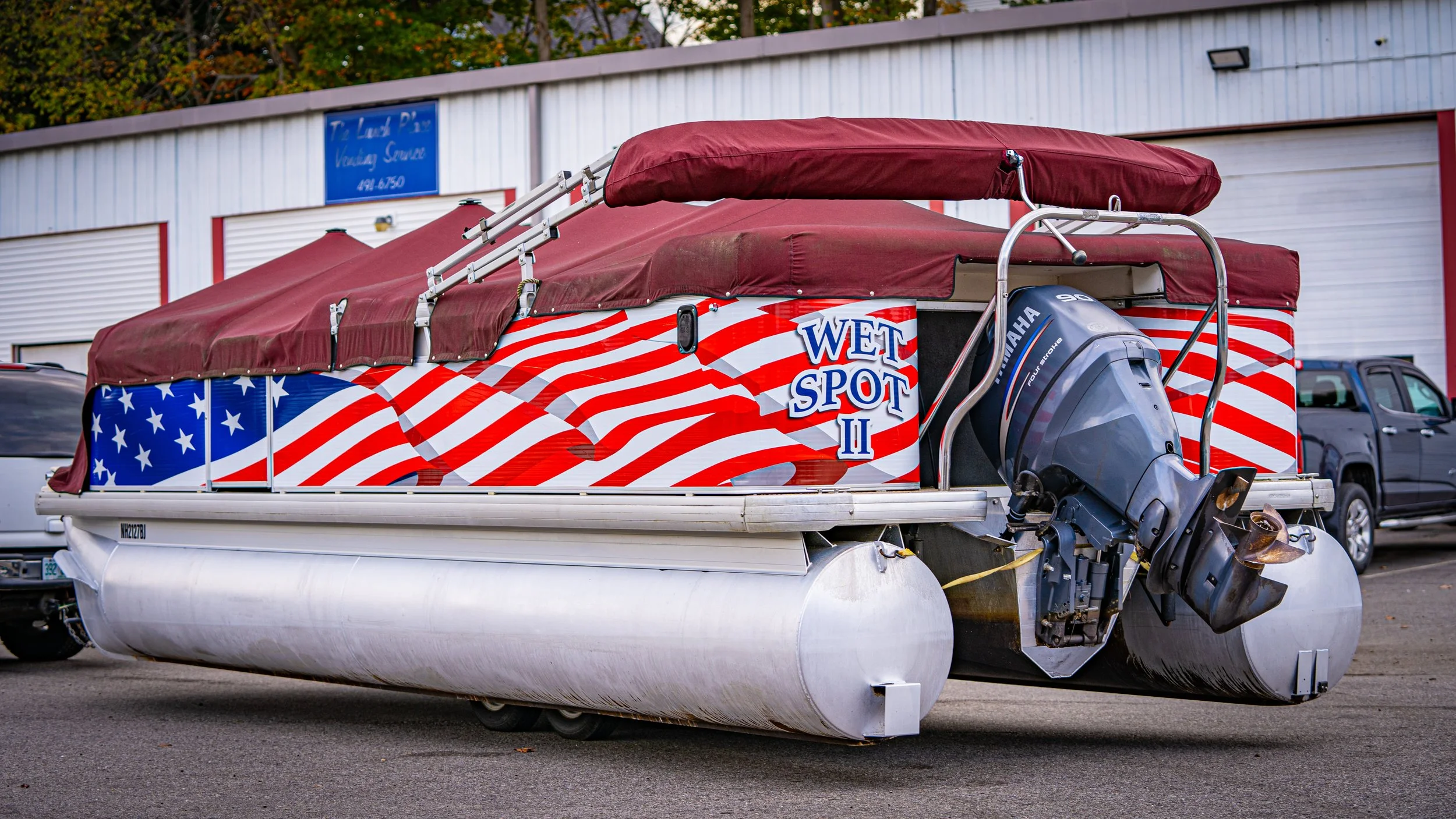 A boat with patriotic American flag design and the words "Wet Spot II" on the side, parked on a trailer in a parking lot.