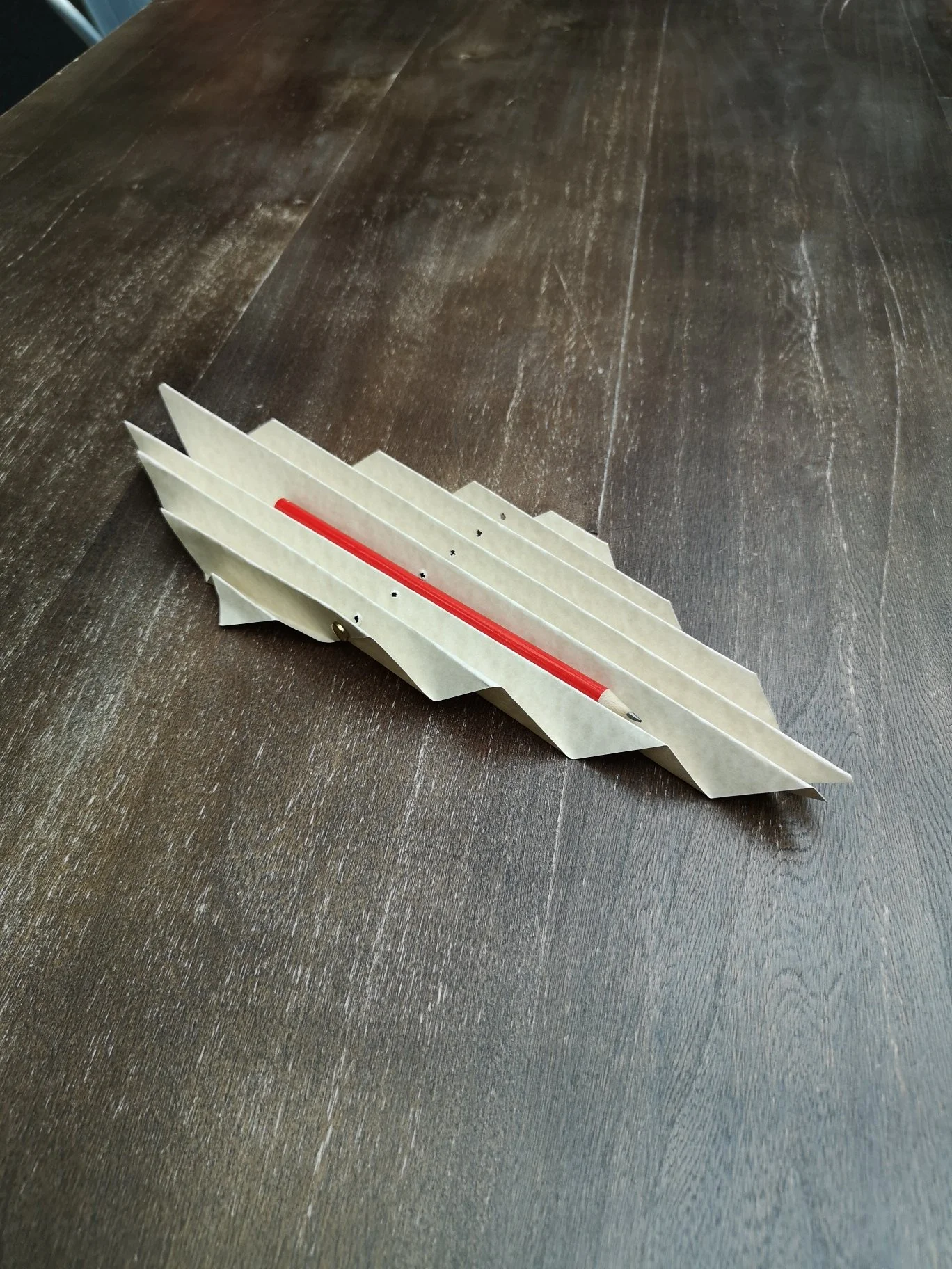 Modello di aeroplano di carta bianco con striscia rossa su tavolo di legno scuro.
