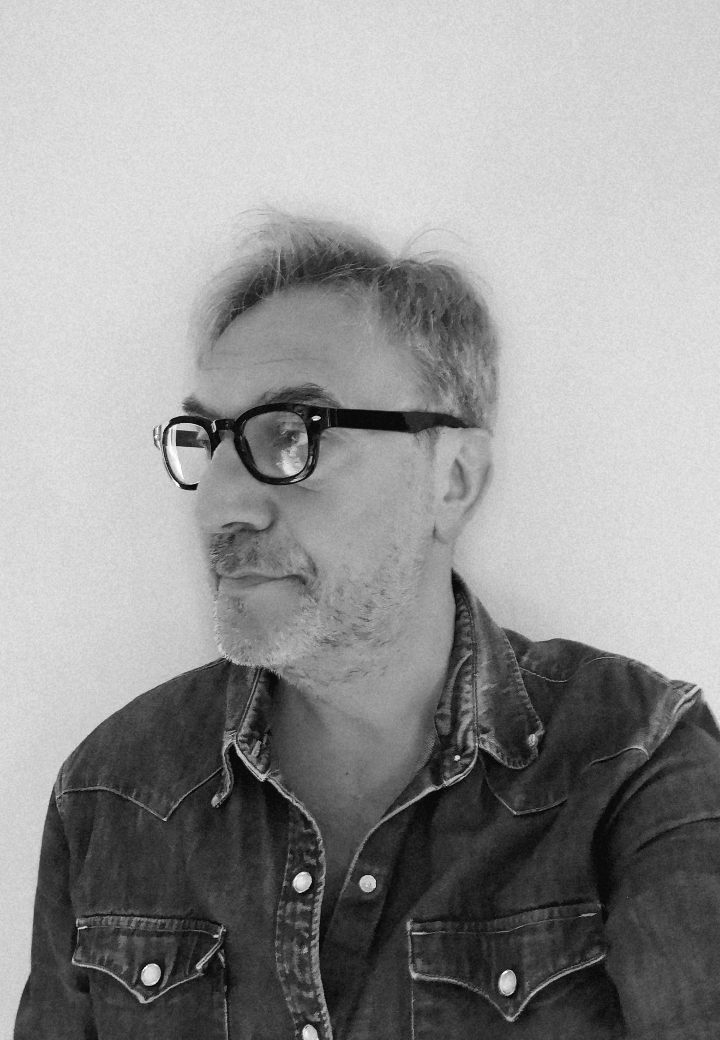 Ritratto in bianco e nero di un uomo con barba, occhiali e camicia scura.