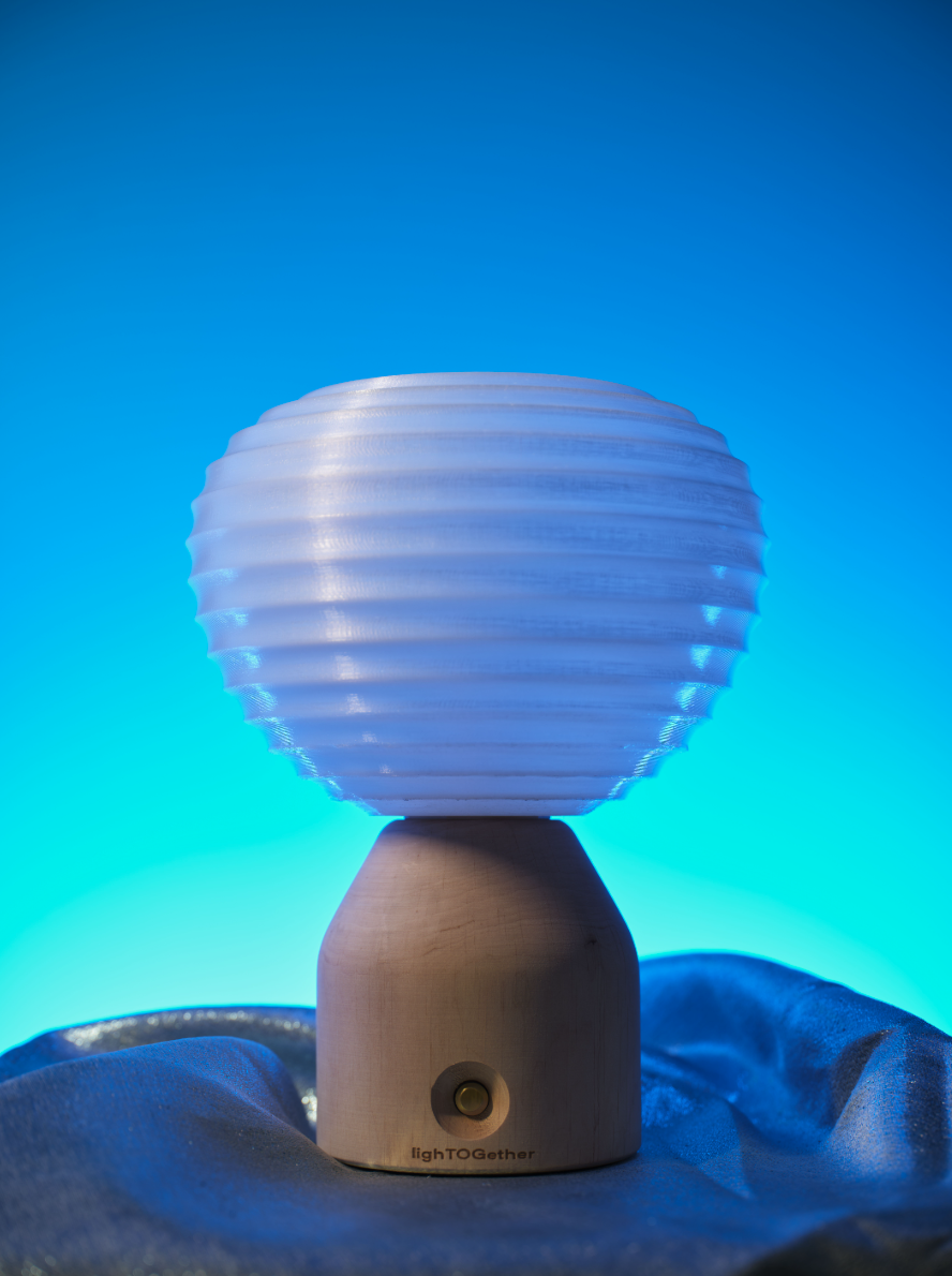 Lampada da tavolo in legno con paralume sferico bianco scanalato, fotografata su tessuto blu con sfondo sfumato azzurro.