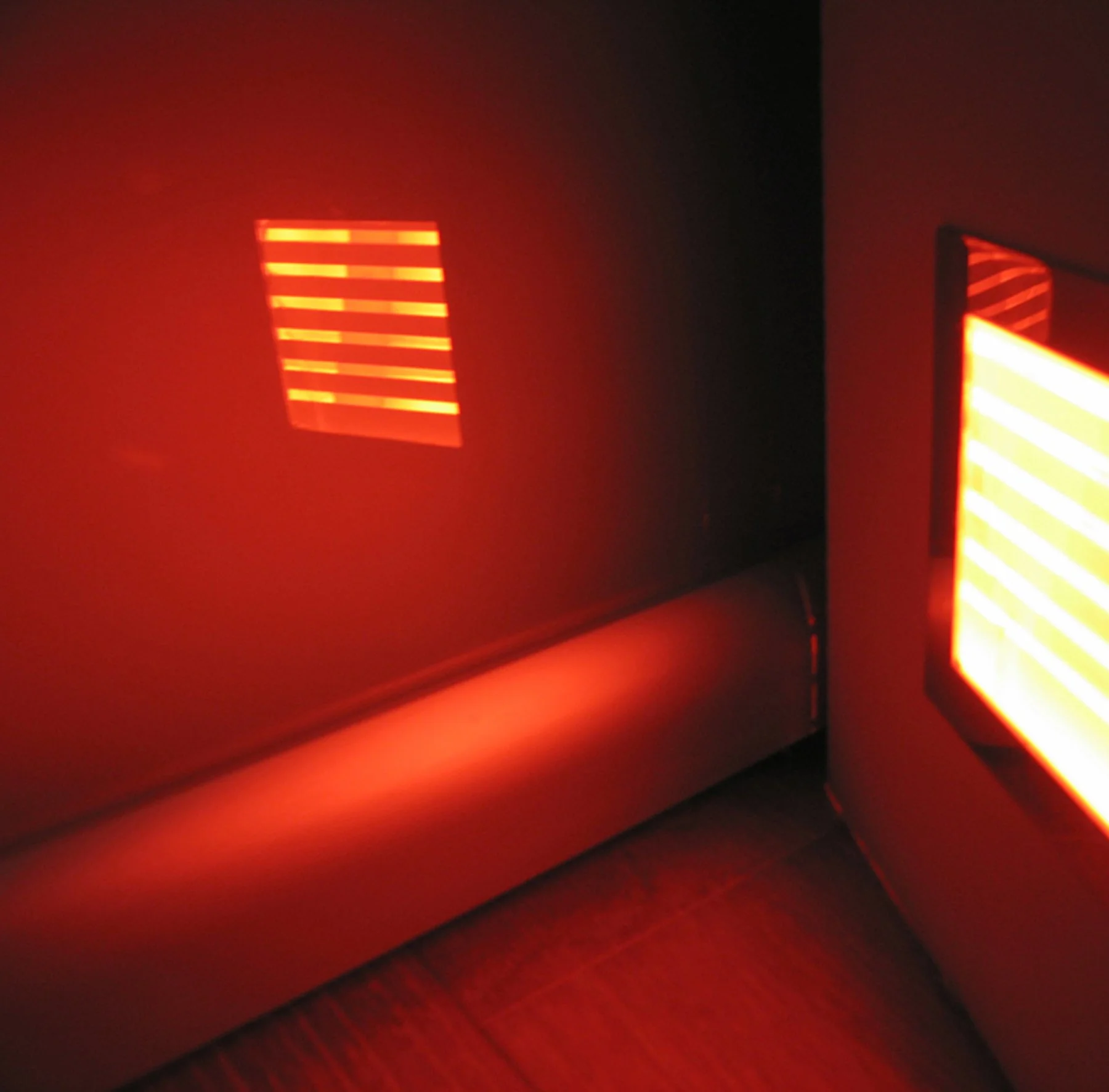 Interno moderno illuminato da luce rossa, con finestre a persiana che proiettano strisce luminose sulle pareti e sul pavimento.