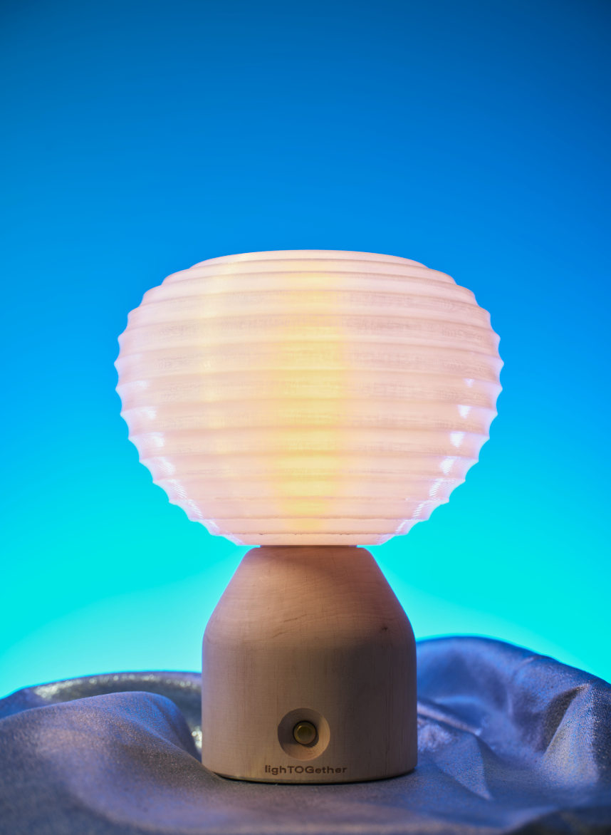 Lampada da tavolo in legno con paralume sferico luminoso su tessuto blu, davanti a uno sfondo sfumato azzurro e turchese.