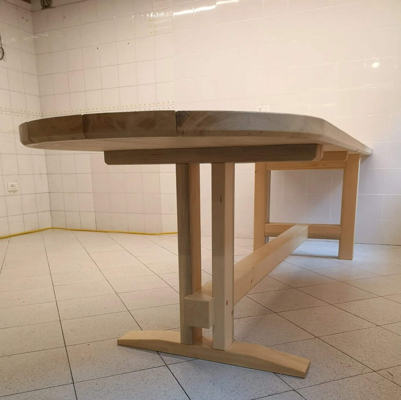 Struttura in legno con ampio piano curvo rialzato, sostenuta da gambe e traverse, in una stanza piastrellata.