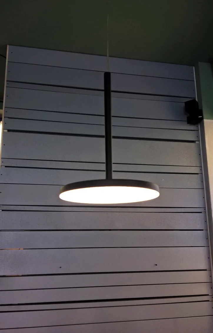 Lampada a sospensione ovale accesa, fissata a un pannello murale grigio.