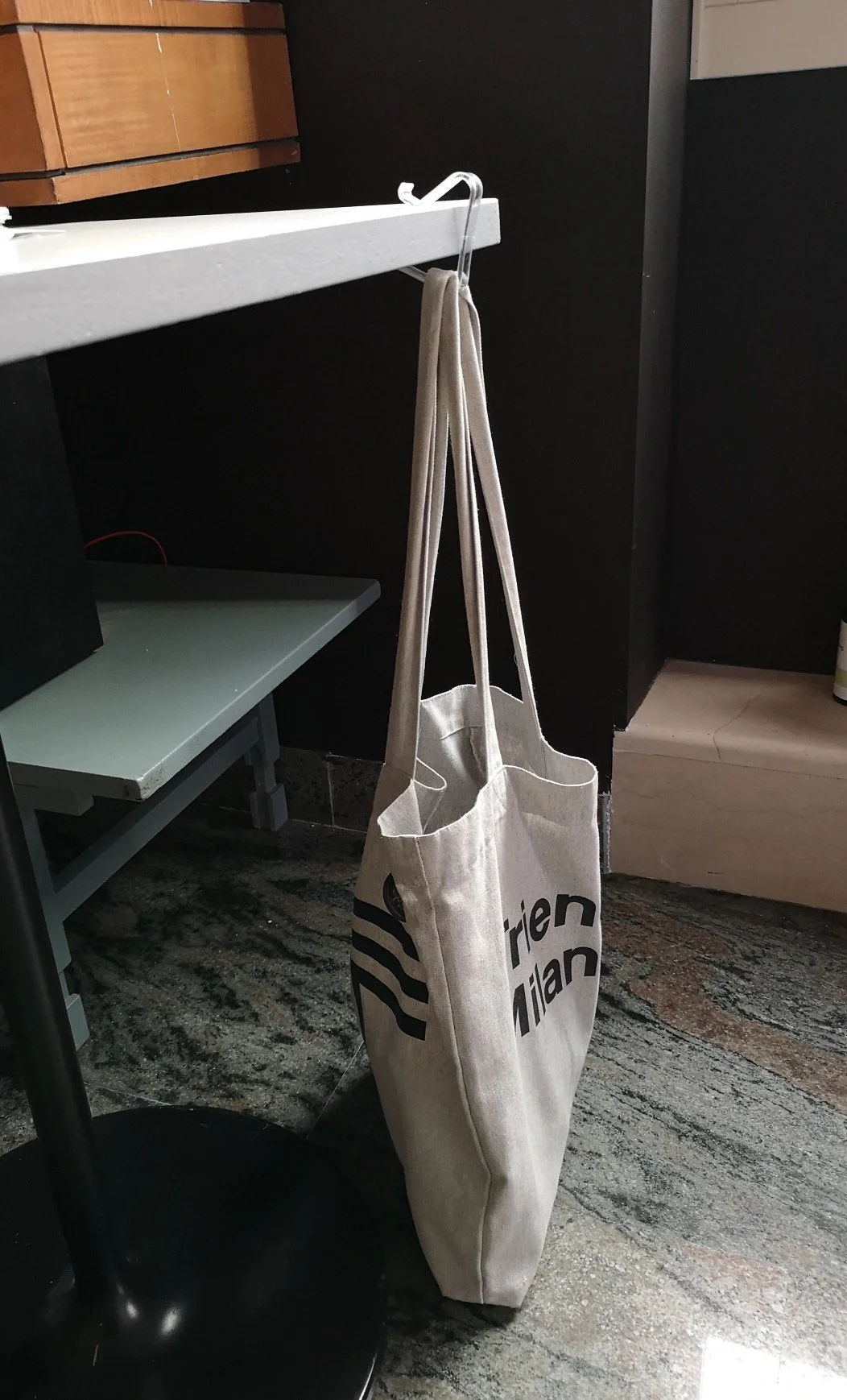 Borsa shopper in tela appesa a un gancio sotto una mensola bianca.