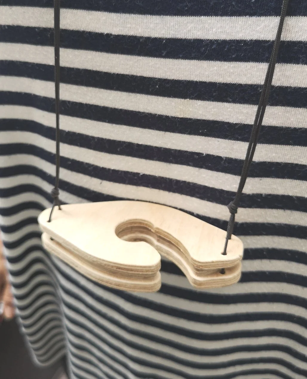 Altalena in legno sospesa con corde nere davanti a uno sfondo a righe bianche e nere.