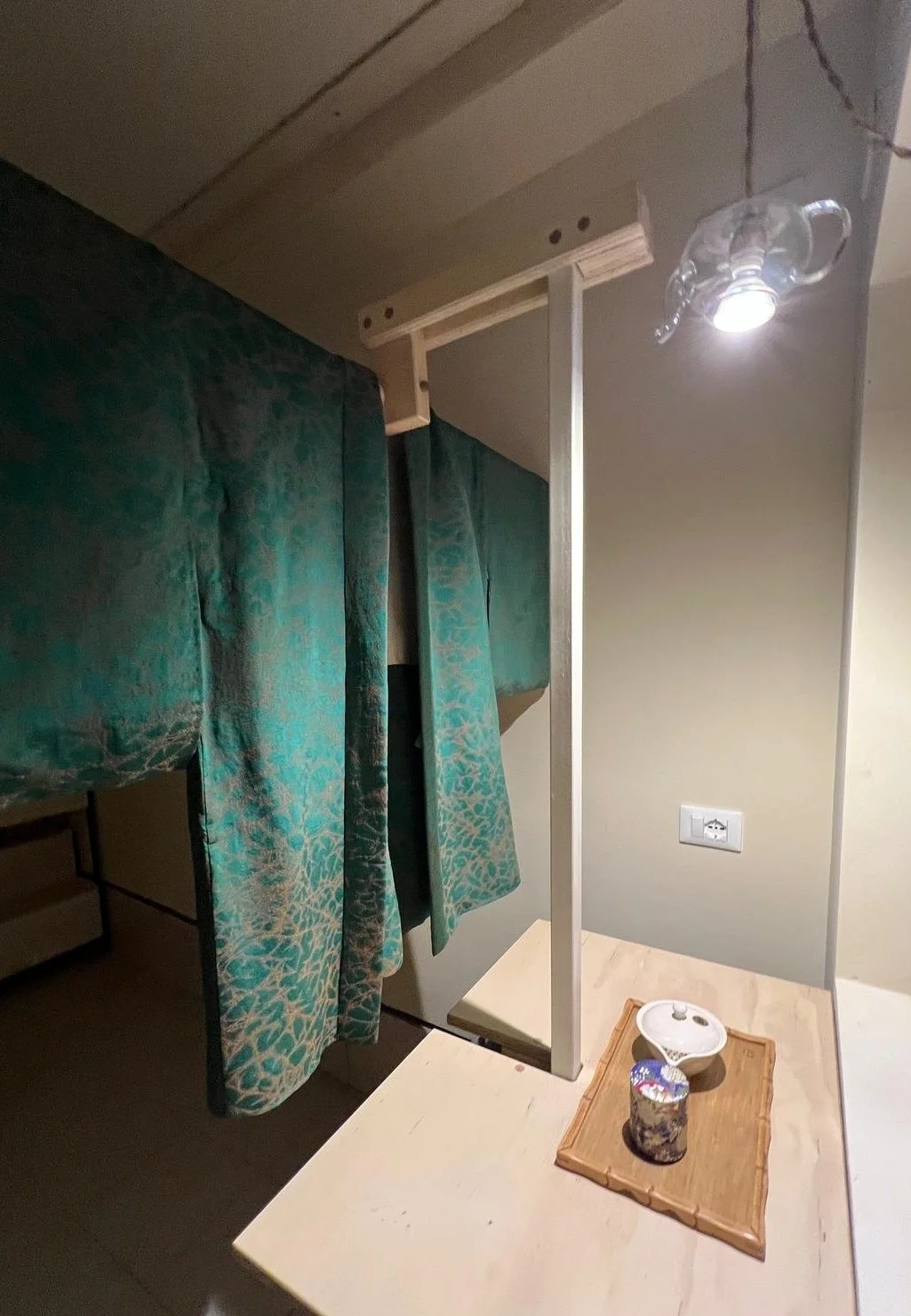 Specchio sopra un tavolo con tenda turchese, lampada a forma di tazza e vassoio con ciotola e barattolo.