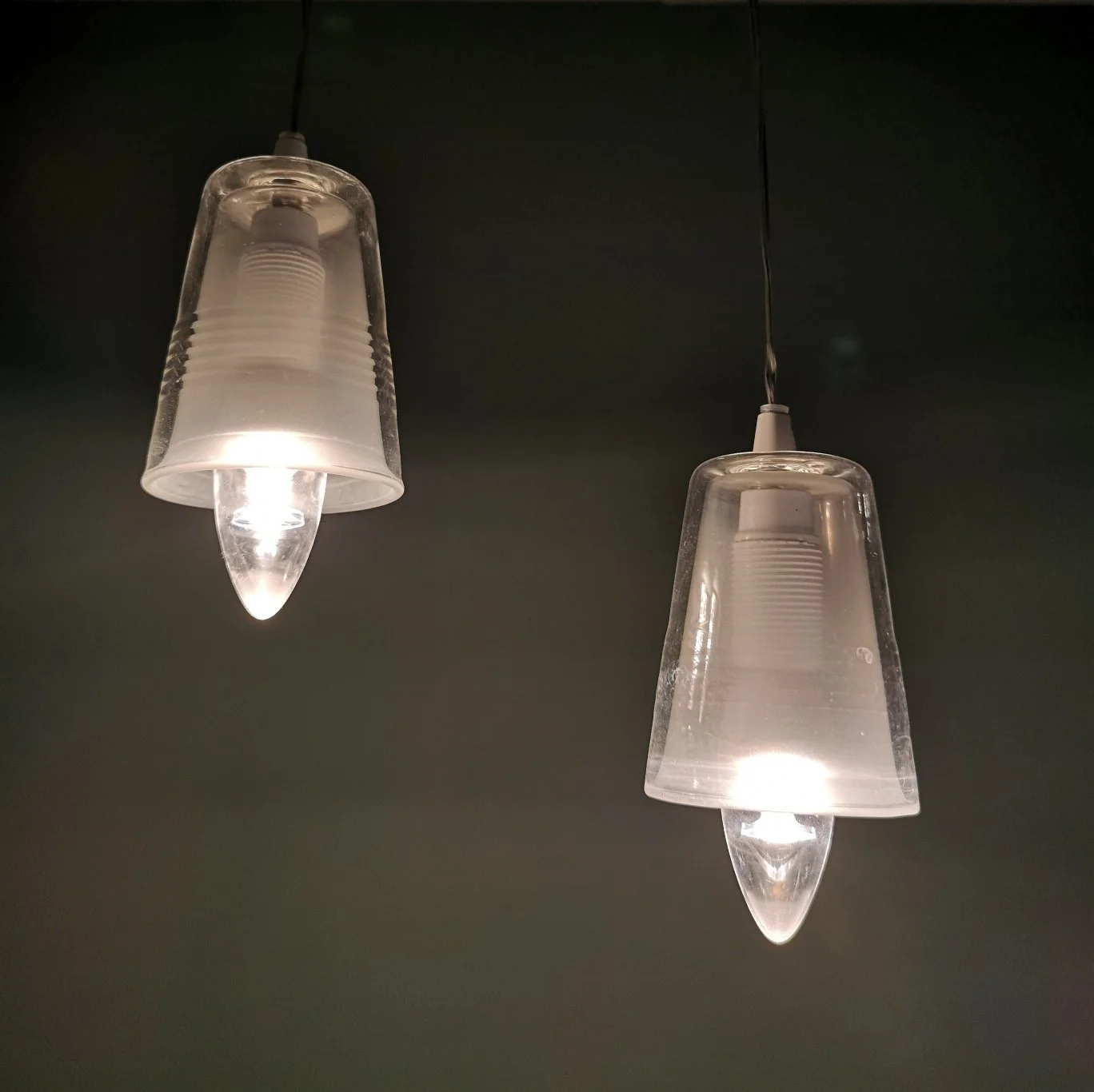 Due lampade a sospensione in vetro trasparente illuminate, su parete scura.