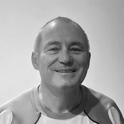 Black and white photo of a smiling man with short hair and a light-colored athletic shirt, standing against a plain background.