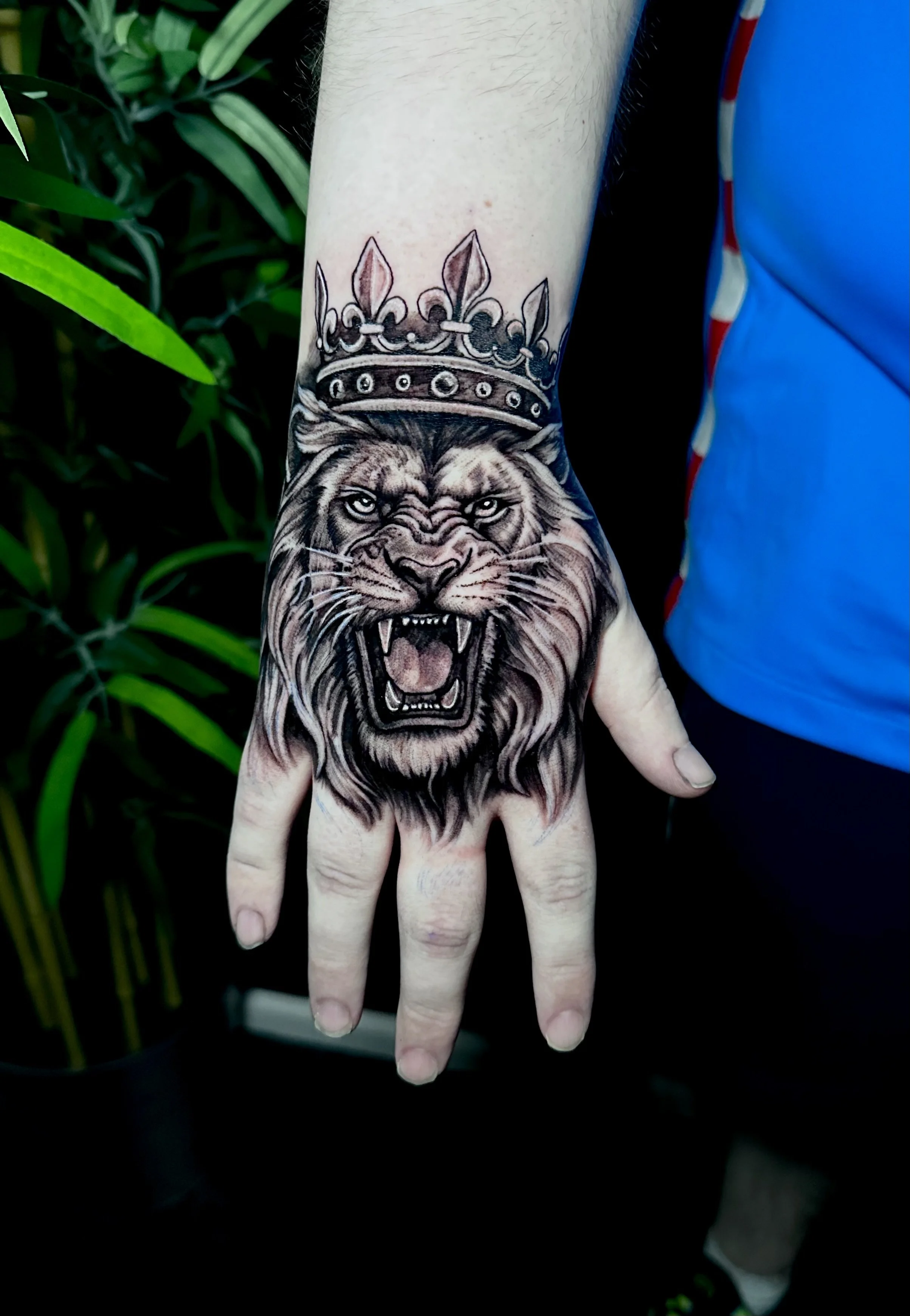 Tattoo of a roaring lion wearing a crown on the hand.