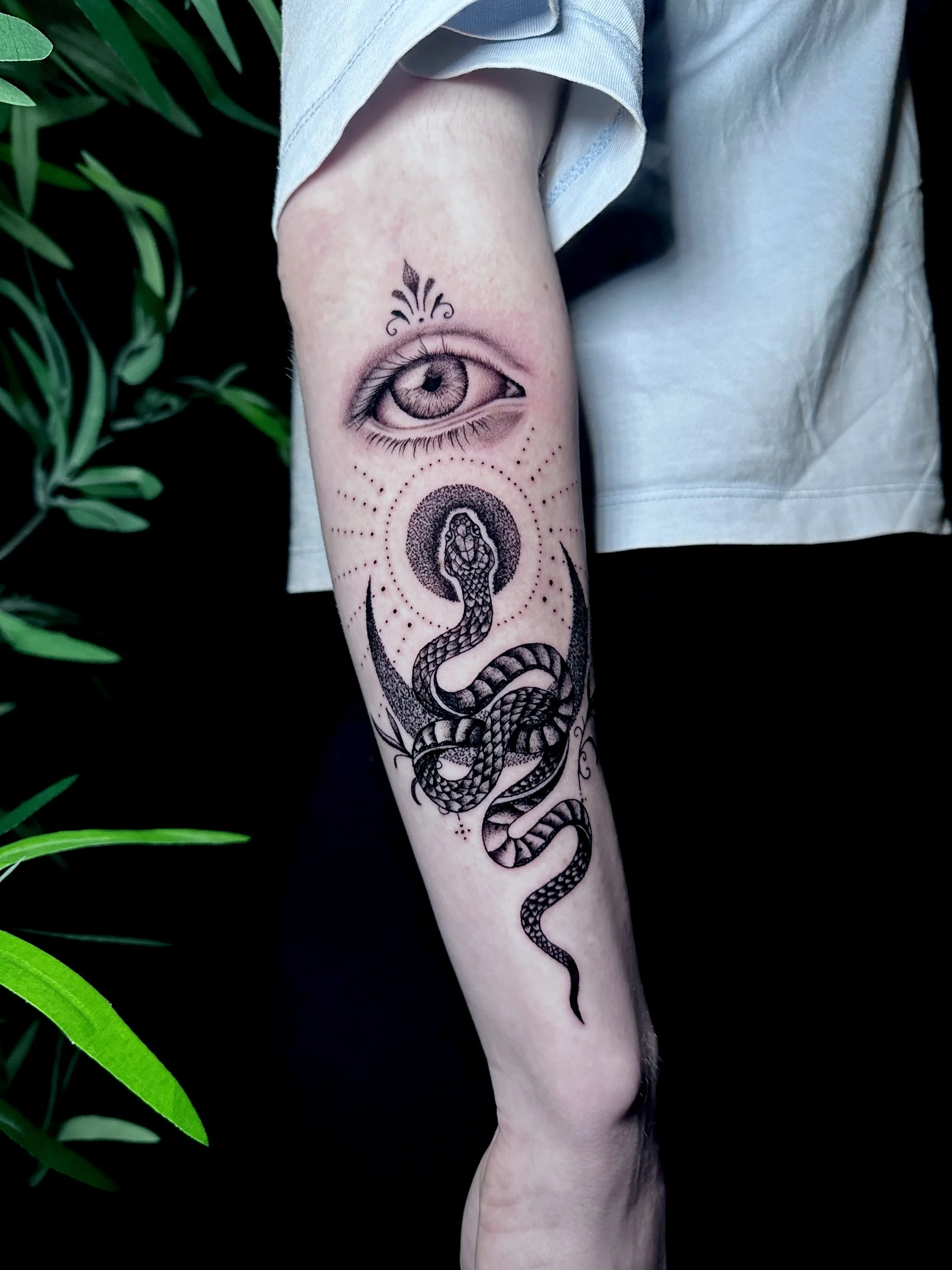Tattoo of a snake with a large eye above it on a person's forearm, with decorative elements and dotted patterns.