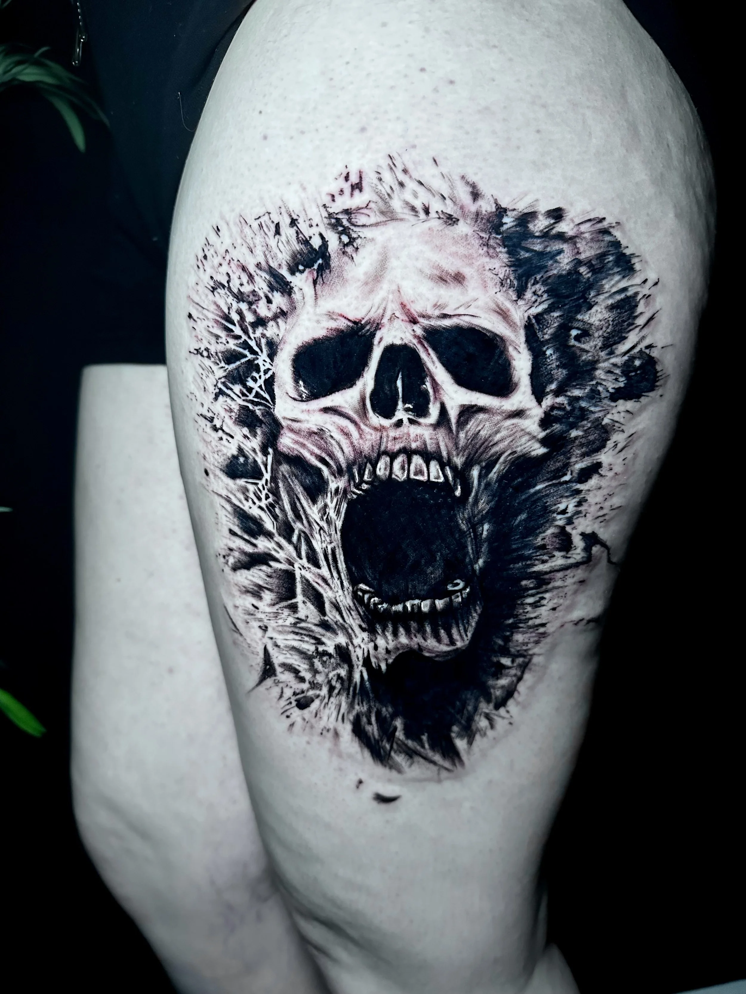 Tattoo of a detailed skull with dark shading and intricate designs on a person's upper arm.