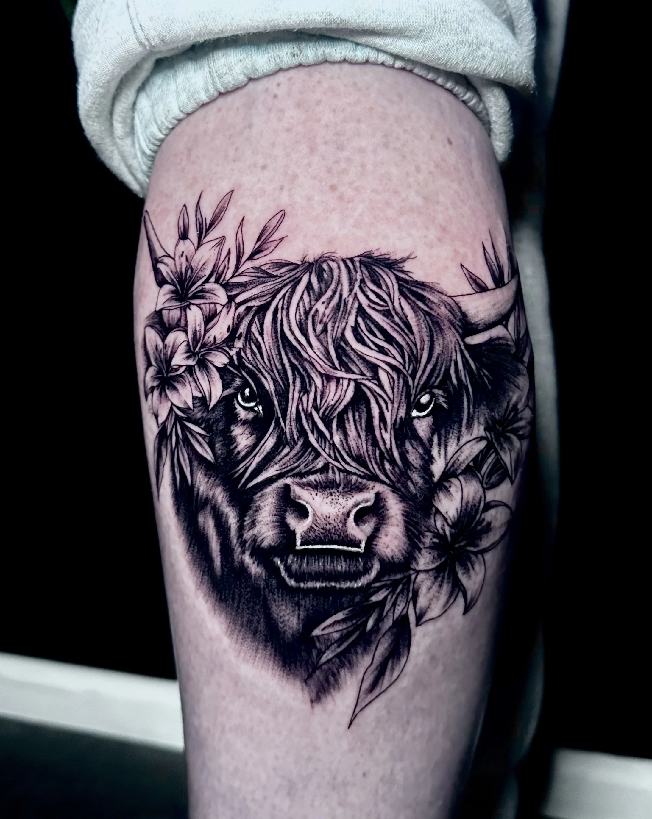 Tattoo of a lion's face with a mane and flowers on the forehead, on a person's arm.
