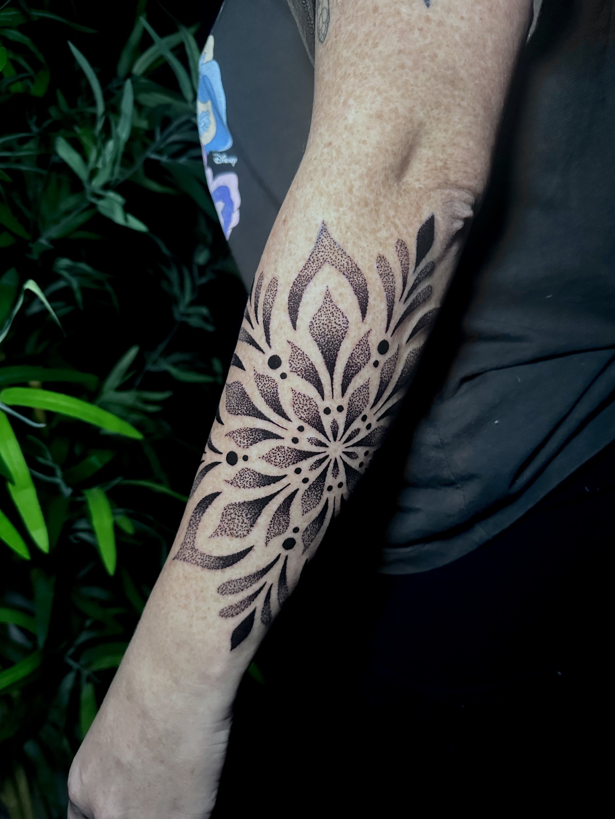 Close-up of a person's arm with a butterfly and floral tattoo design on the forearm, next to some green foliage.