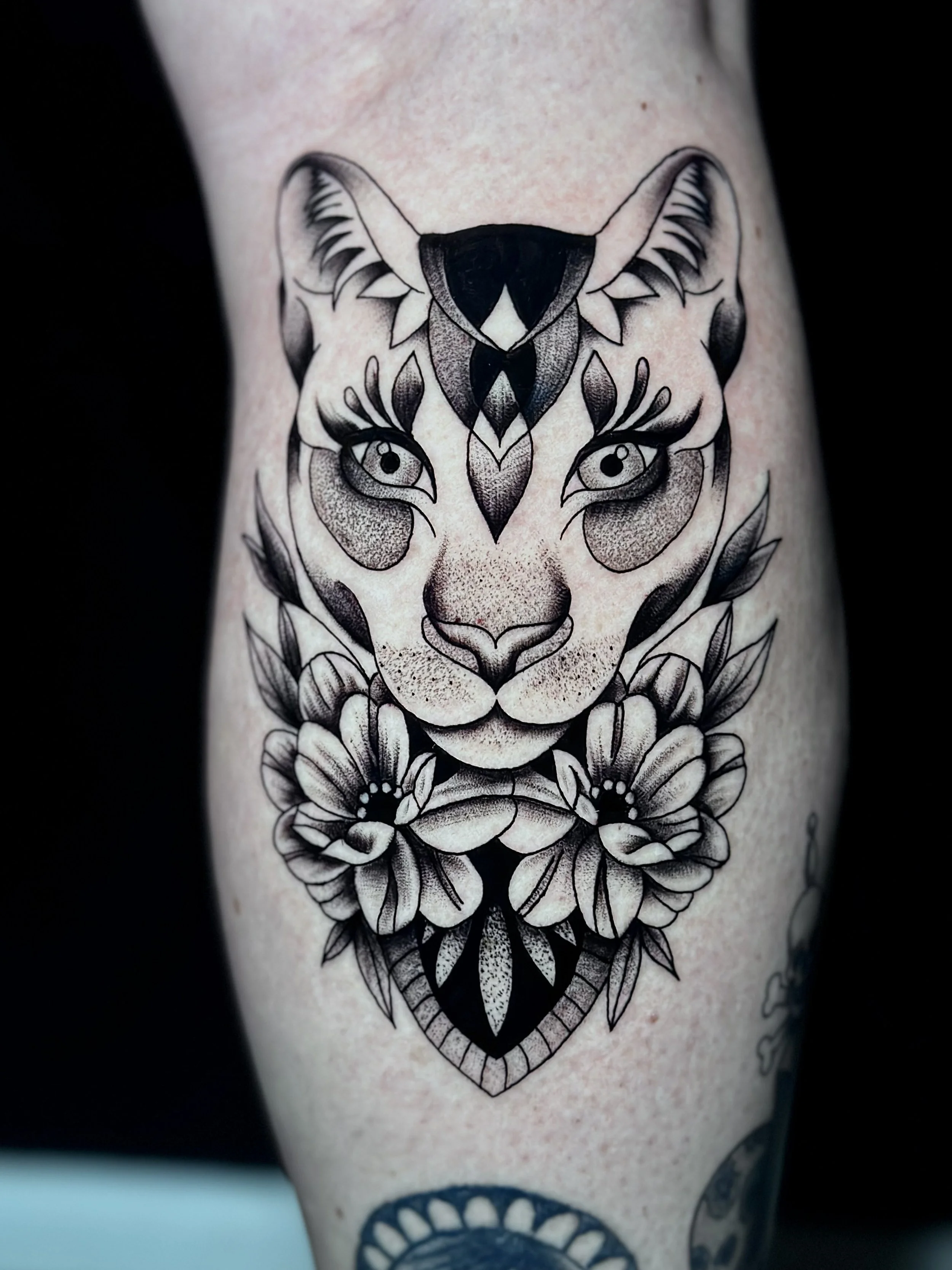 Black and gray tattoo of a heart with a stylized owl face, surrounded by floral and leaf designs on skin.