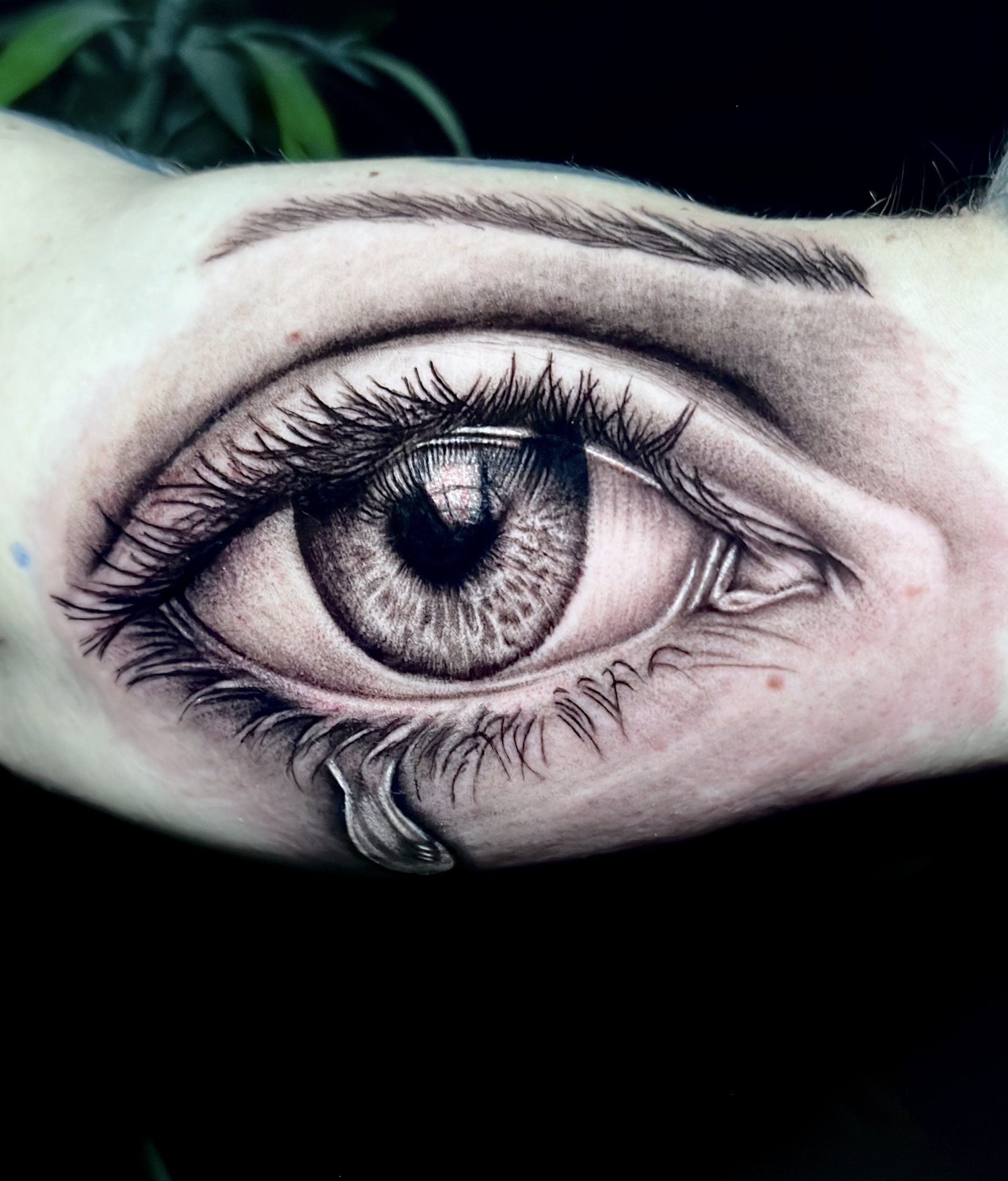Close-up of a human eye with detailed eyelashes, eyelid, and a dark iris, set against a black background.