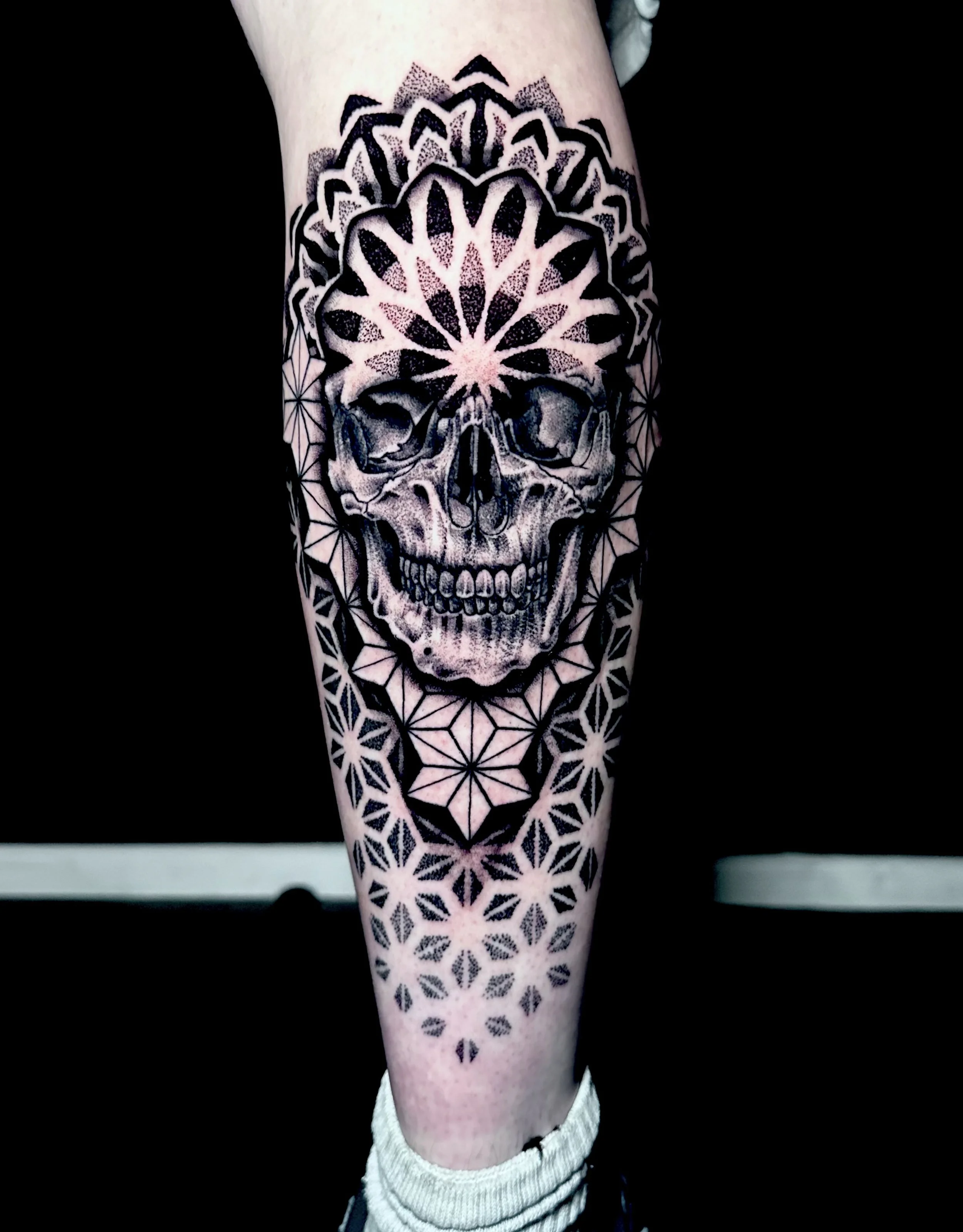 Tattoo of a detailed skull with geometric and floral patterns on a person's arm.