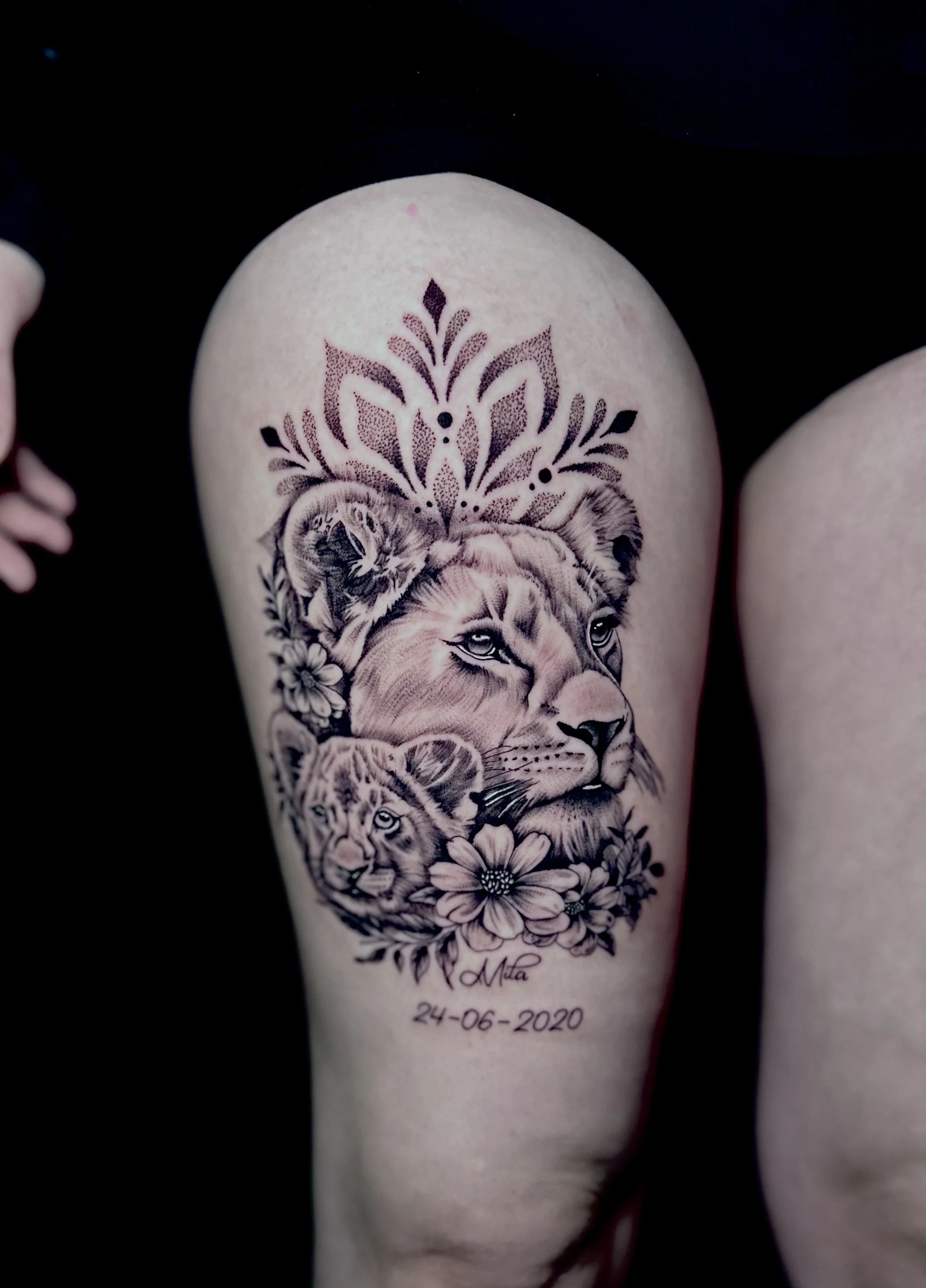 Tattoo of a lion with detailed face and expressive eyes, surrounded by floral patterns and feathers. The tattoo includes a signature "Mta" and a date "24-06-2020" at the bottom.