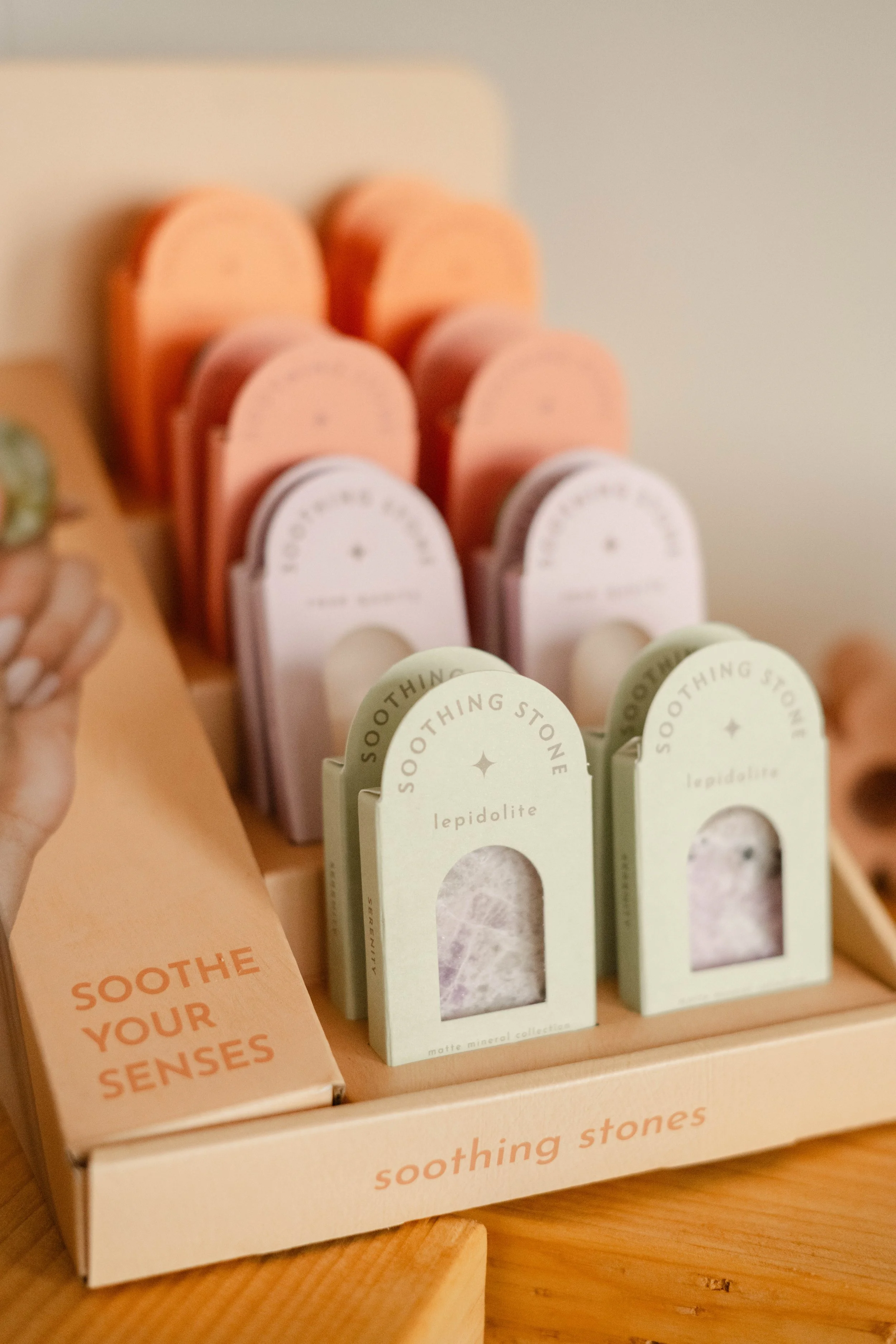 Display of mineral collection named 'Soothe your senses' with various pastel-colored boxes and packages of mineral stones, including lepidolite.