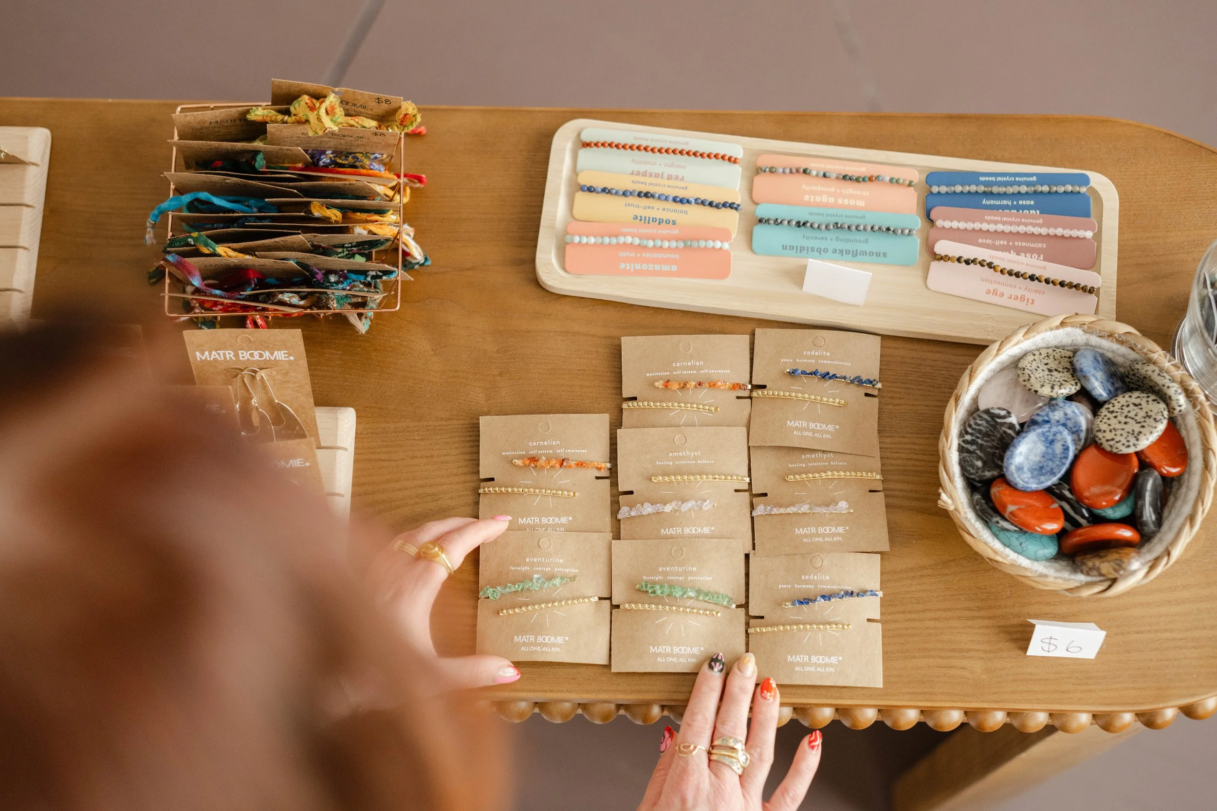 Display of jewelry including bracelets and earrings on a wooden table, with hand pointing to some of the items.