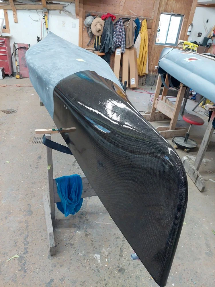 A workshop with a partially assembled sleek, black fiber-glass boat on stands, with tools and work materials around.
