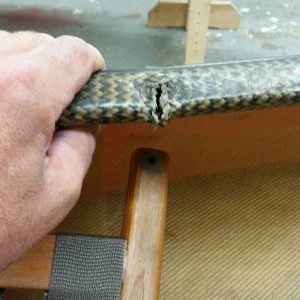 Close-up of a hand holding a broken piece of a carbon fiber skateboard deck with the damage visible.