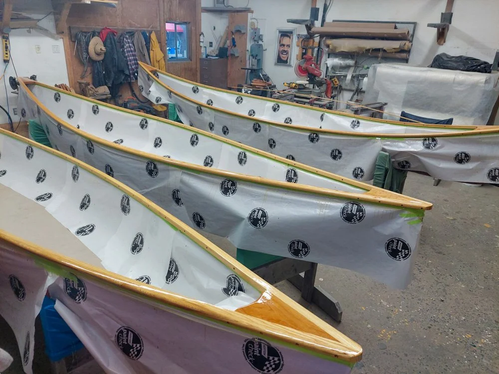 Workshop with several wooden kayaks covered with protective plastic and sitting on workbenches.