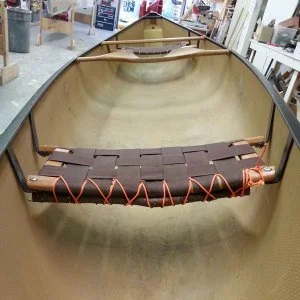 Inside view of a wooden canoe with a brown seat and orange cords, located in a store.