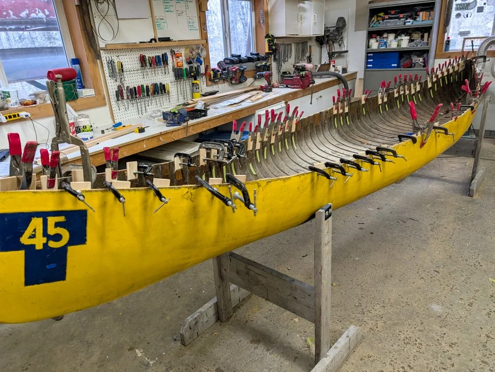 Yellow kayak with the number 45 on the side, being assembled in a workshop with clamps attaching the frame.