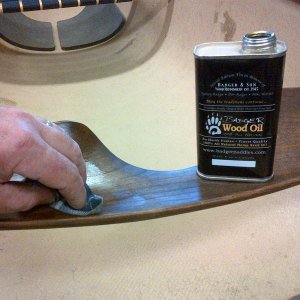 Person applying teak oil to a wooden surface with a cloth, with a bottle of teak wood oil nearby.