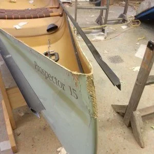 Close-up of a boat with visible damage to the hull, labeled 'Inspector 15', in a workshop or repair area.