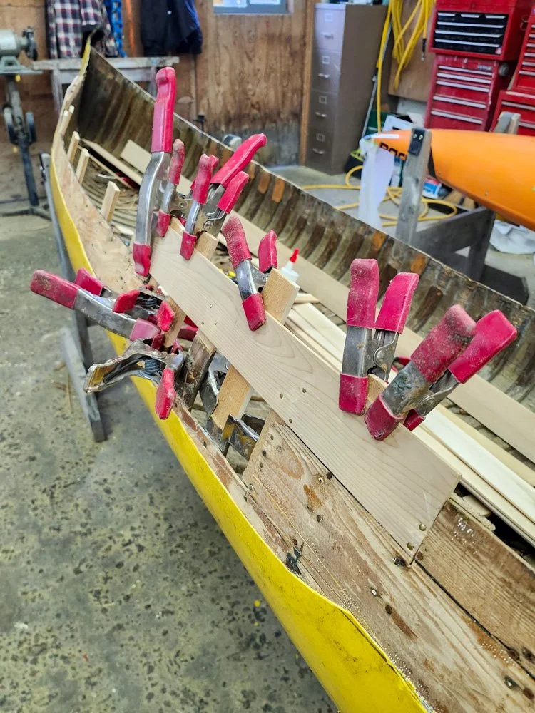 Clamps holding wooden planks in place on a boat under construction or repair in a workshop.